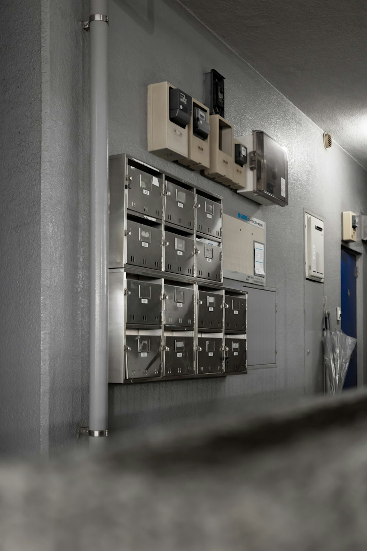 Briefkästen und Stromzähler-Einheiten an einer Wand in einem schwach beleuchteten Flur montiert