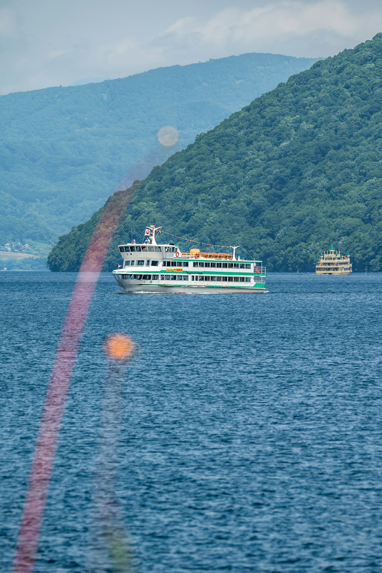 Kapal wisata berlayar di danau dengan pegunungan hijau di latar belakang