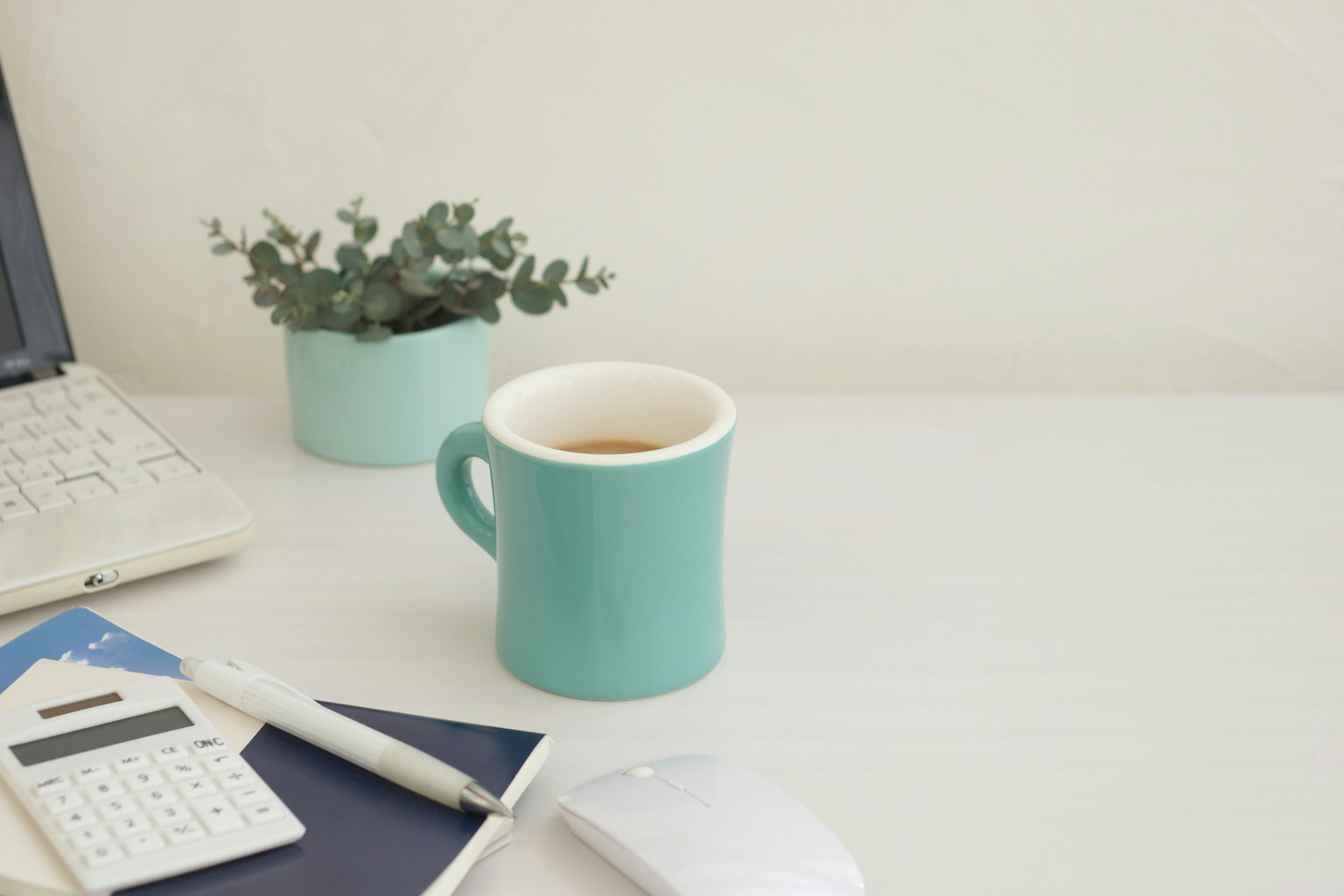 Eine Schreibtischszene mit einer teal Tasse Kaffee und einer Topfpflanze