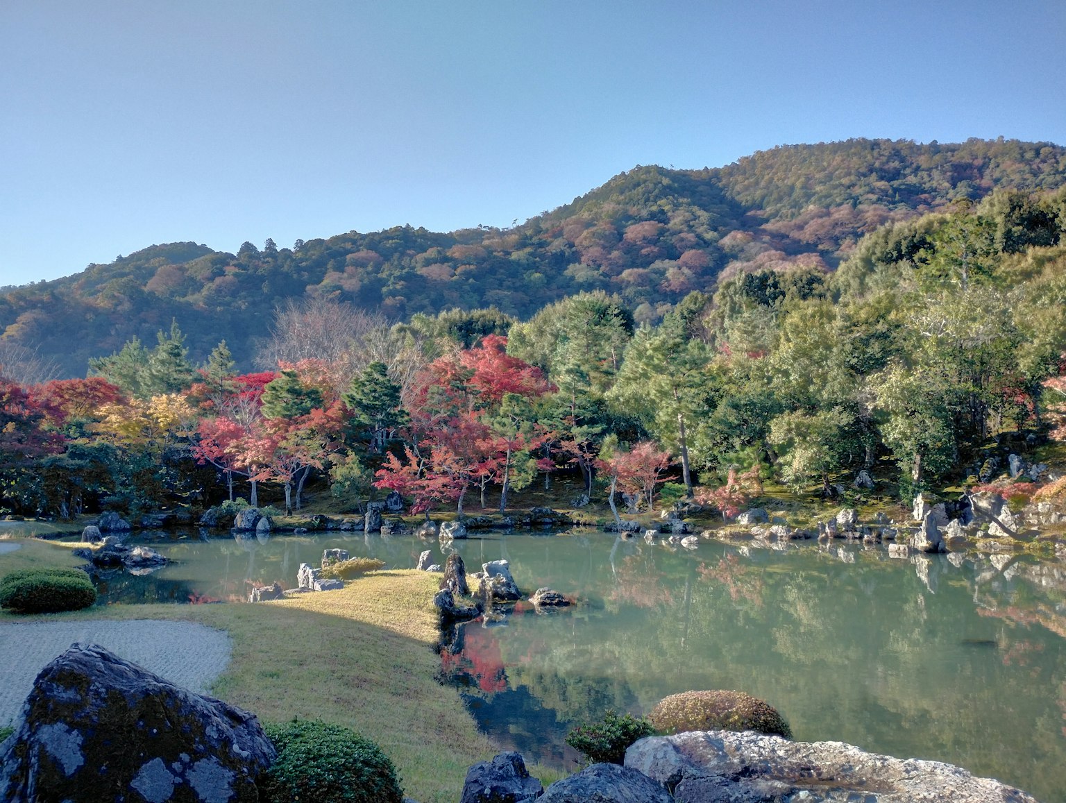 Vista panoramica di un giardino giapponese con foglie autunnali e uno stagno tranquillo sullo sfondo delle montagne