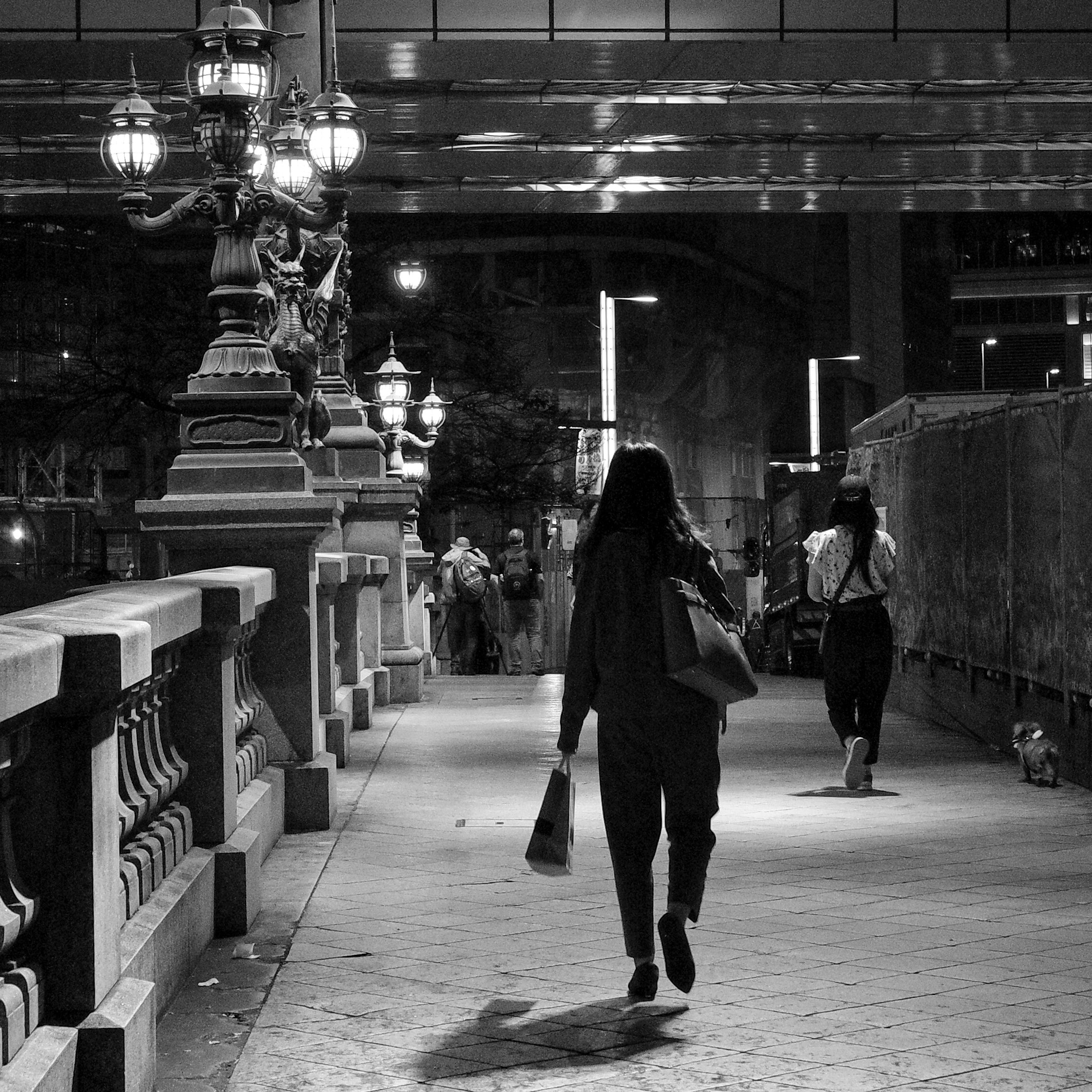 silhouettes of people walking along a stone colonnade at night