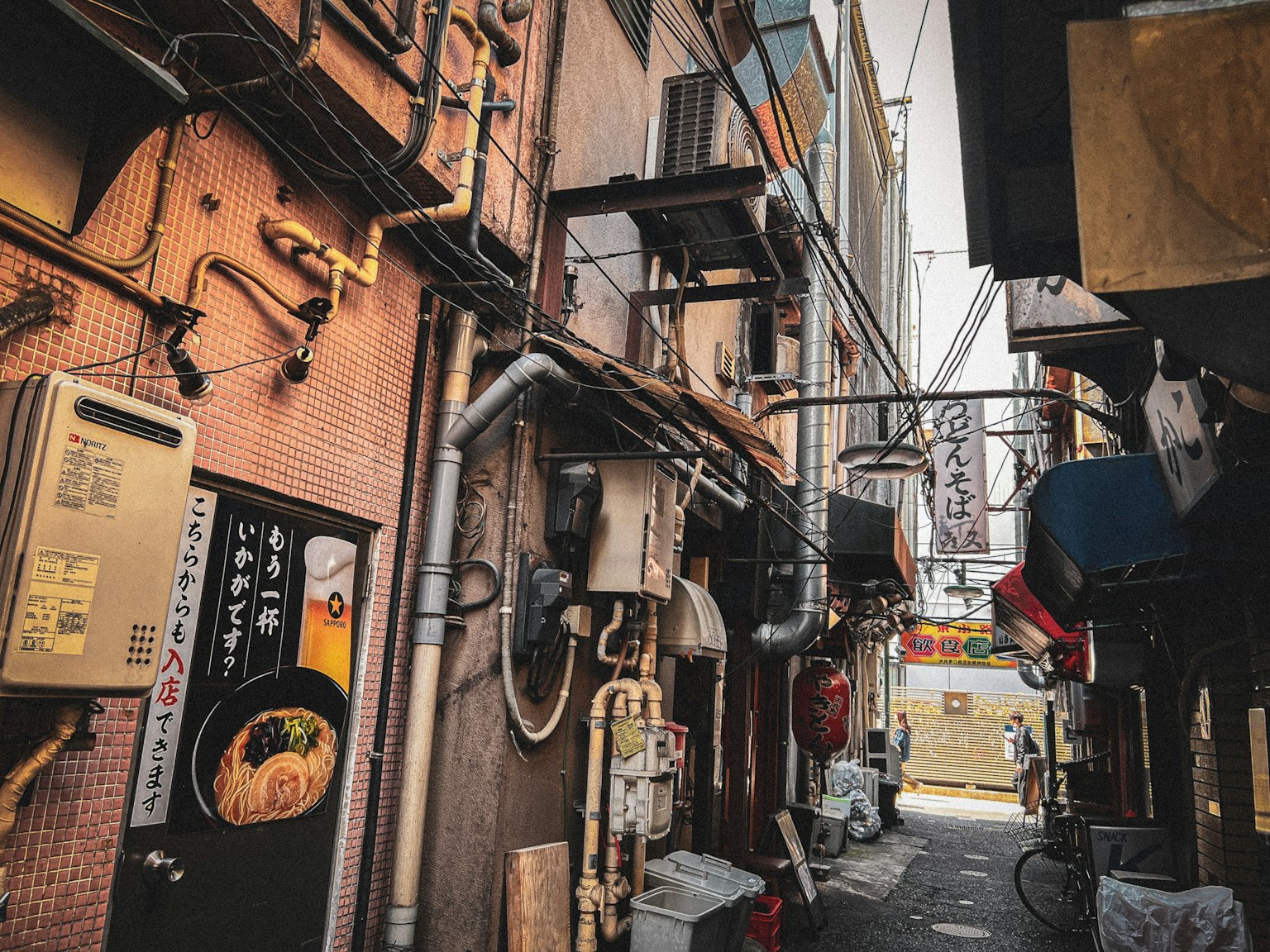 狭い路地に沿った建物の外観と配管が見える