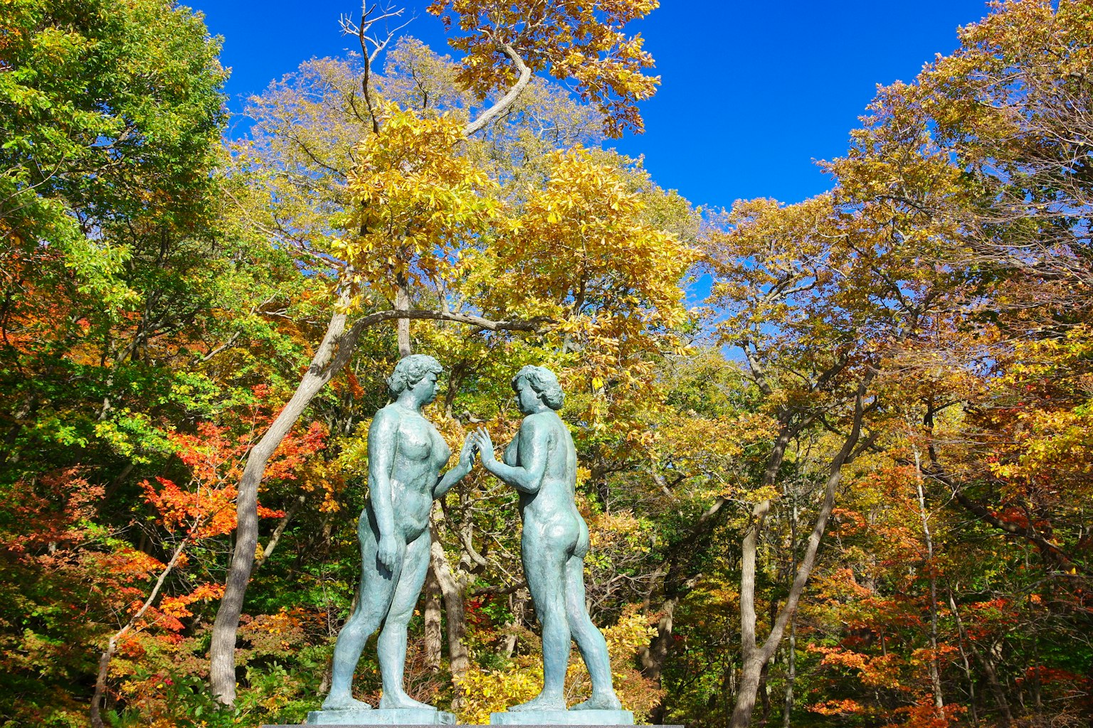 Due statue che si ergono sotto un cielo blu circondate da foglie autunnali