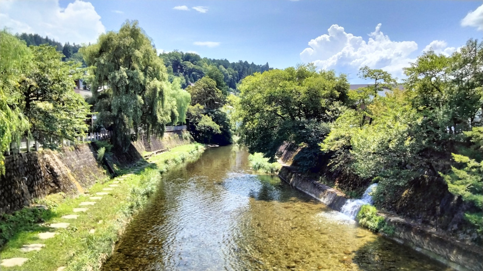 Lush riverside scenery with waterfalls under a blue sky