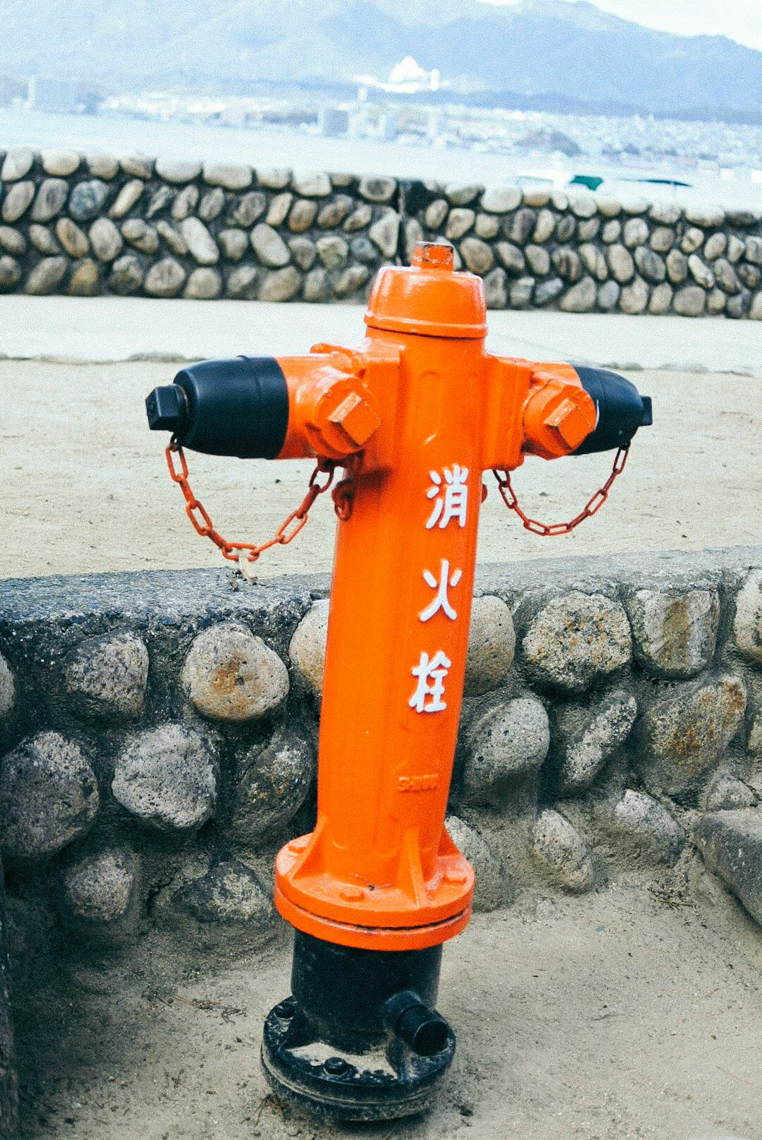 Sebuah hydrant oranye berdiri di depan dinding batu