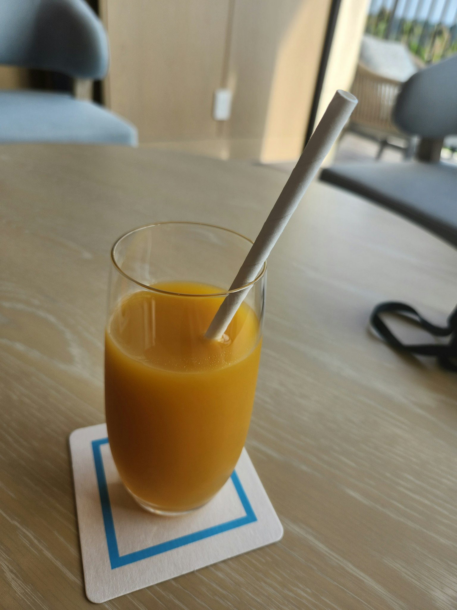 Sebuah gelas jus jeruk dengan sedotan di atas tatakan gelas di meja