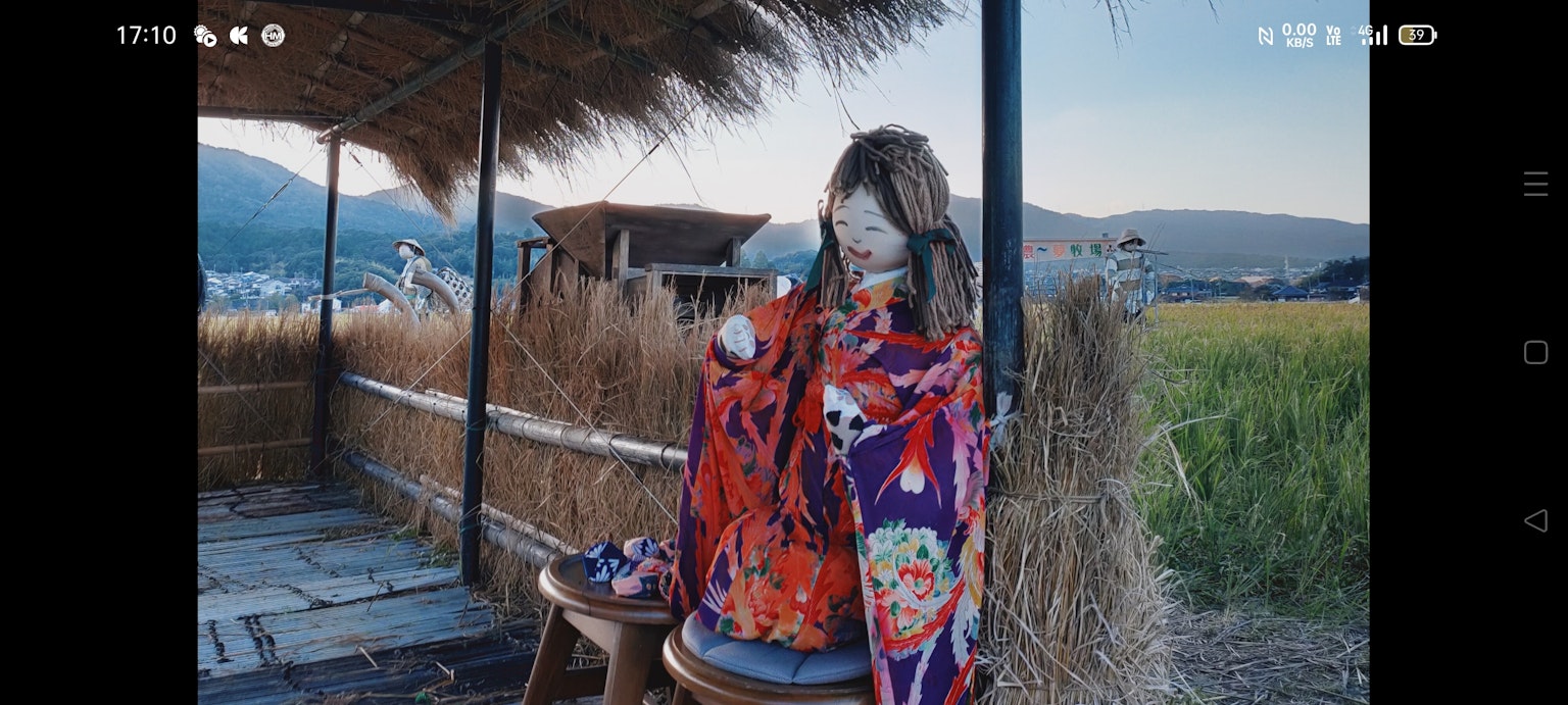 Une femme en kimono coloré assise devant une cabane en chaume entourée d'herbe