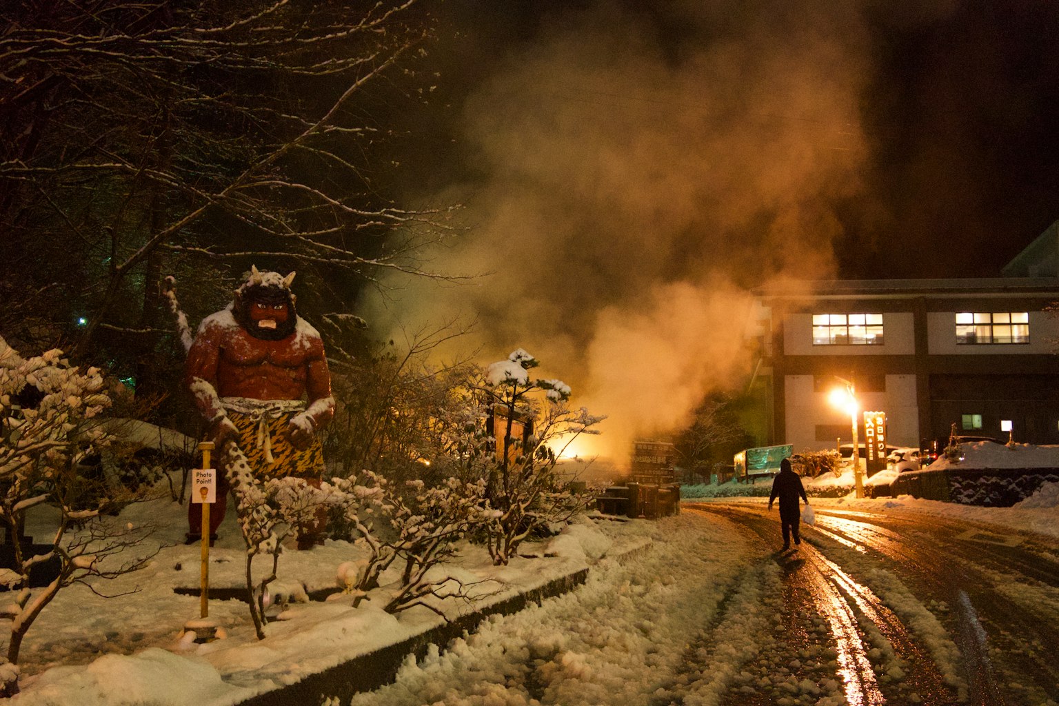 Scène nocturne dans une station thermale enneigée avec une statue géante et de la vapeur qui s'élève