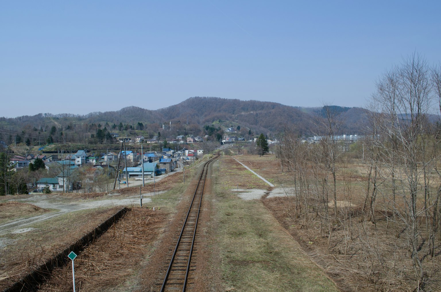 Rural landscape with railway tracks under a clear blue sky and distant mountains