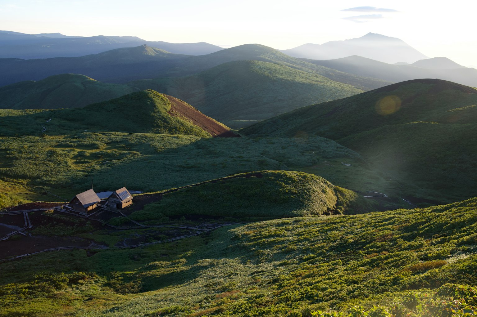 Paesaggio suggestivo con dolci colline verdi e montagne lontane con una piccola capanna