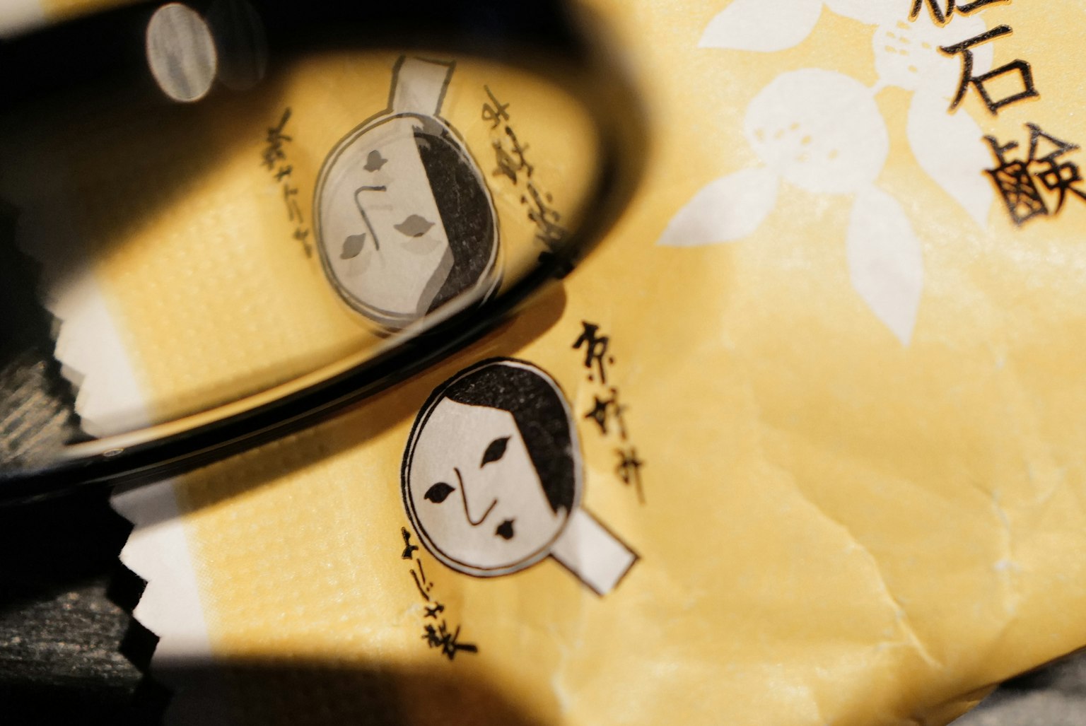 Reflejo de un personaje japonés tradicional en gafas de montura negra sobre un embalaje amarillo