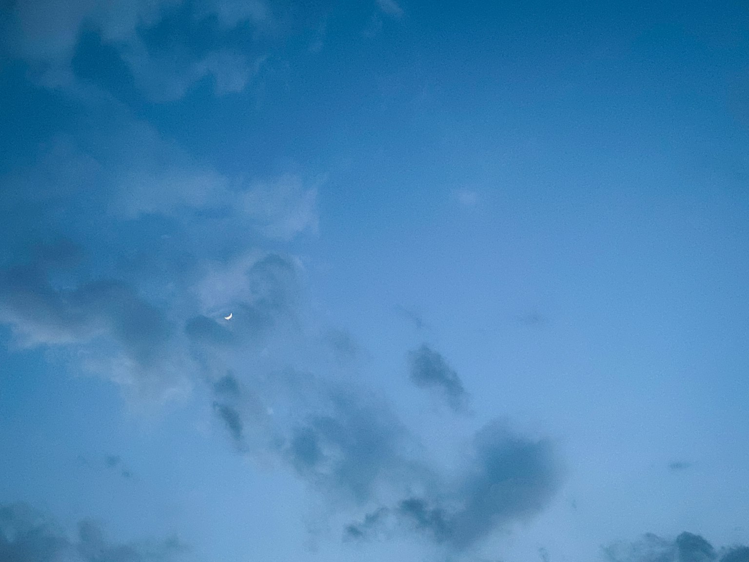 Un cielo blu chiaro con nuvole e una piccola luna che appare