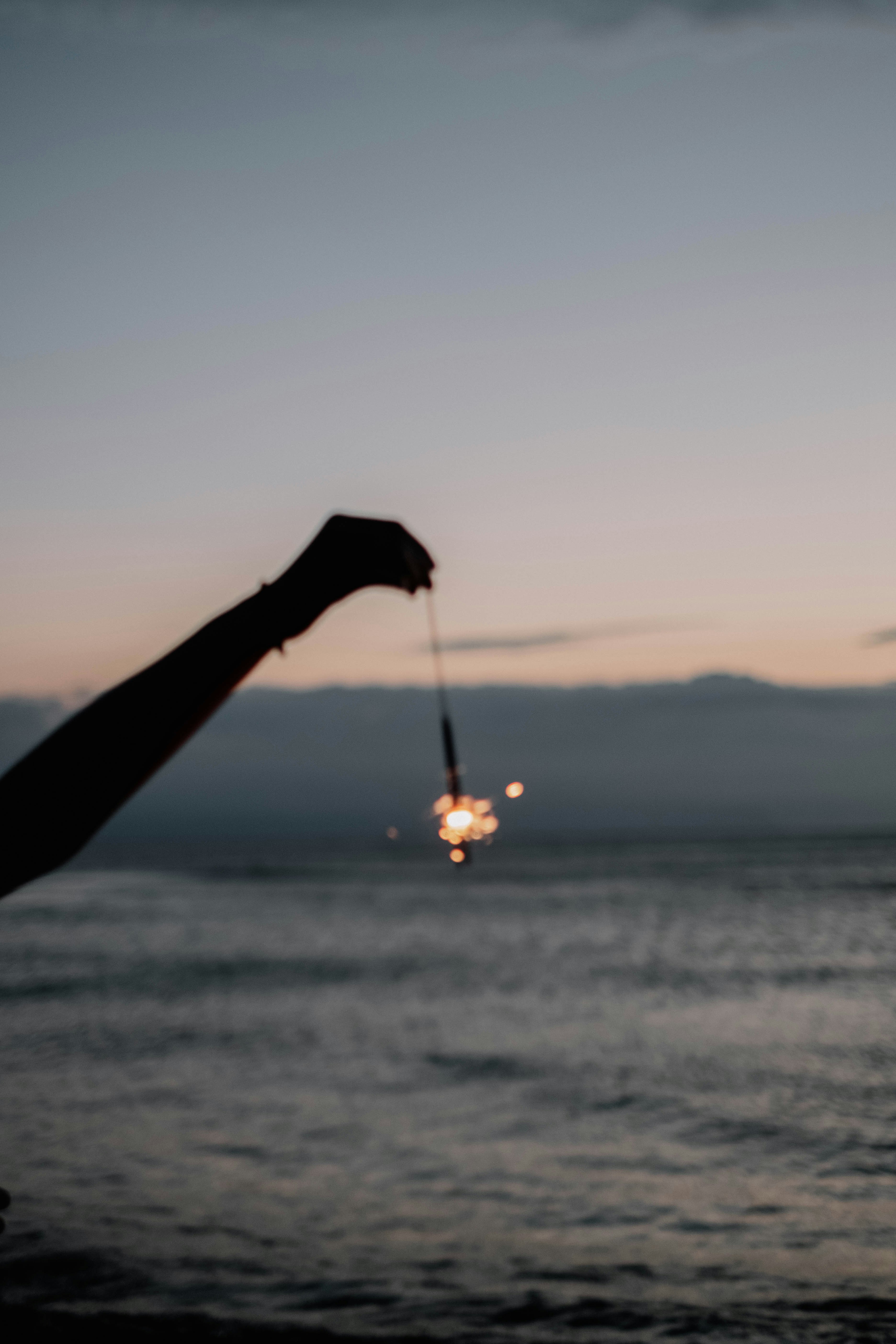 silhouette tendant la main vers des lumières suspendues au bord de la mer au crépuscule