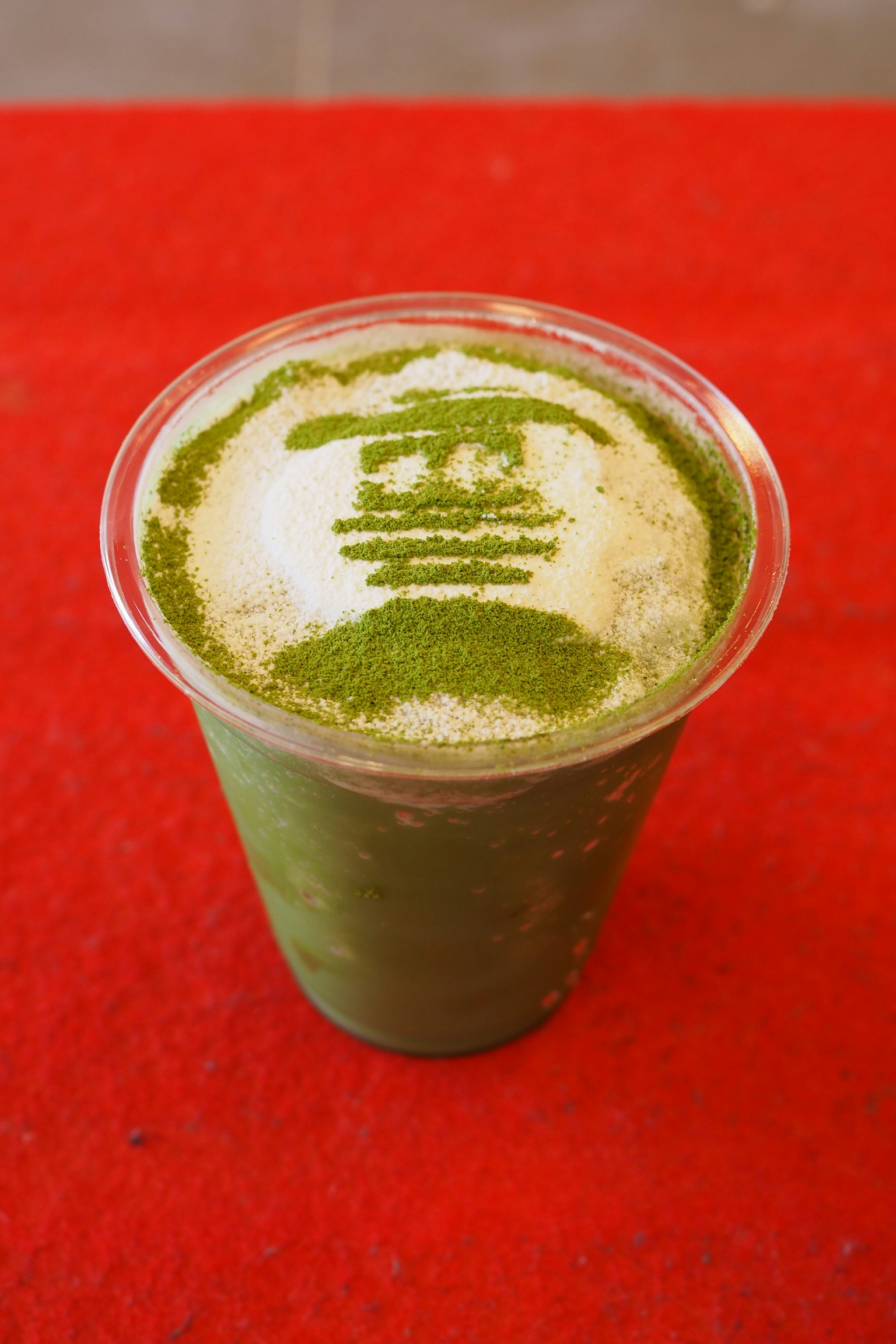 Gobelet transparent de latte au thé vert avec un design artistique en mousse sur le dessus et un fond rouge