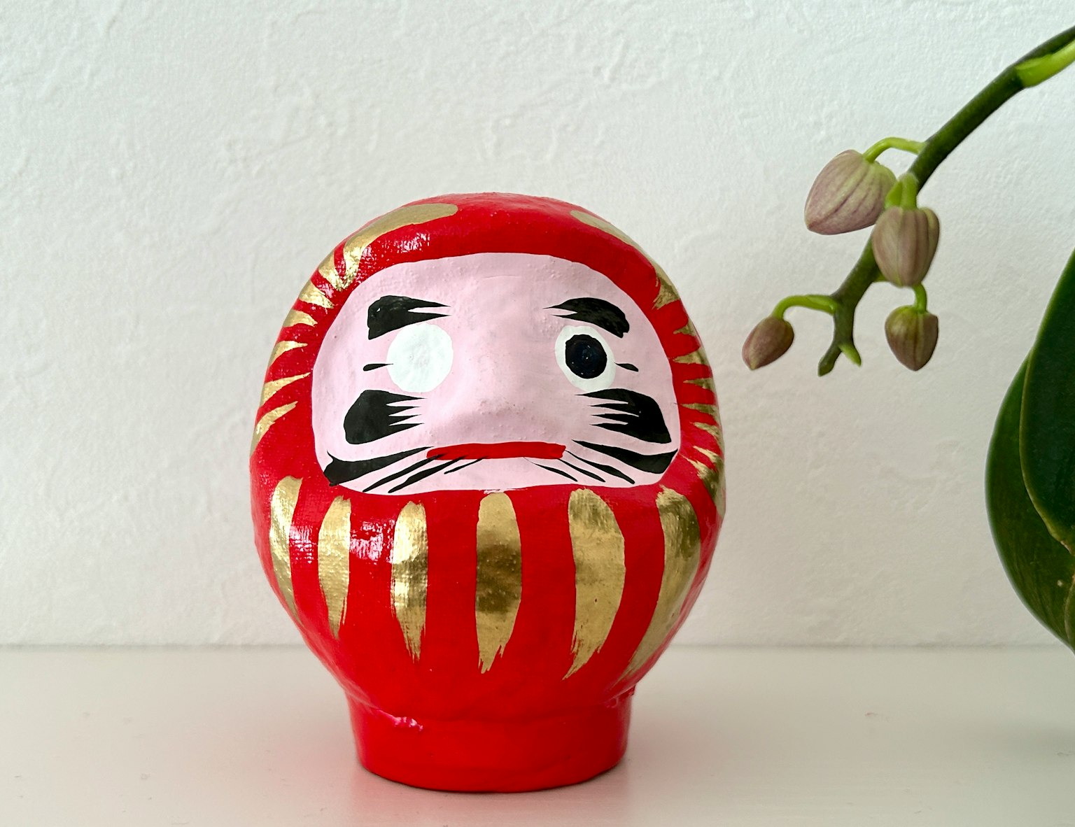 Rote Daruma-Puppe mit Pflanzenhintergrund