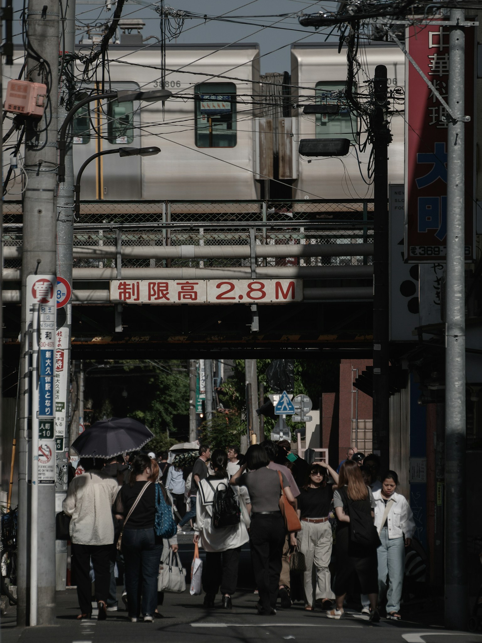 Crowd of people walking under a train track with a height restriction sign reading 2.8 meters