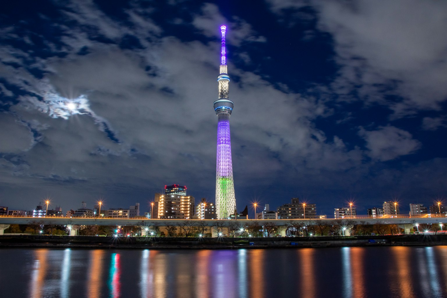 Tokyo Skytree nachts beleuchtet mit bunten Lichtern, die sich im Wasser spiegeln
