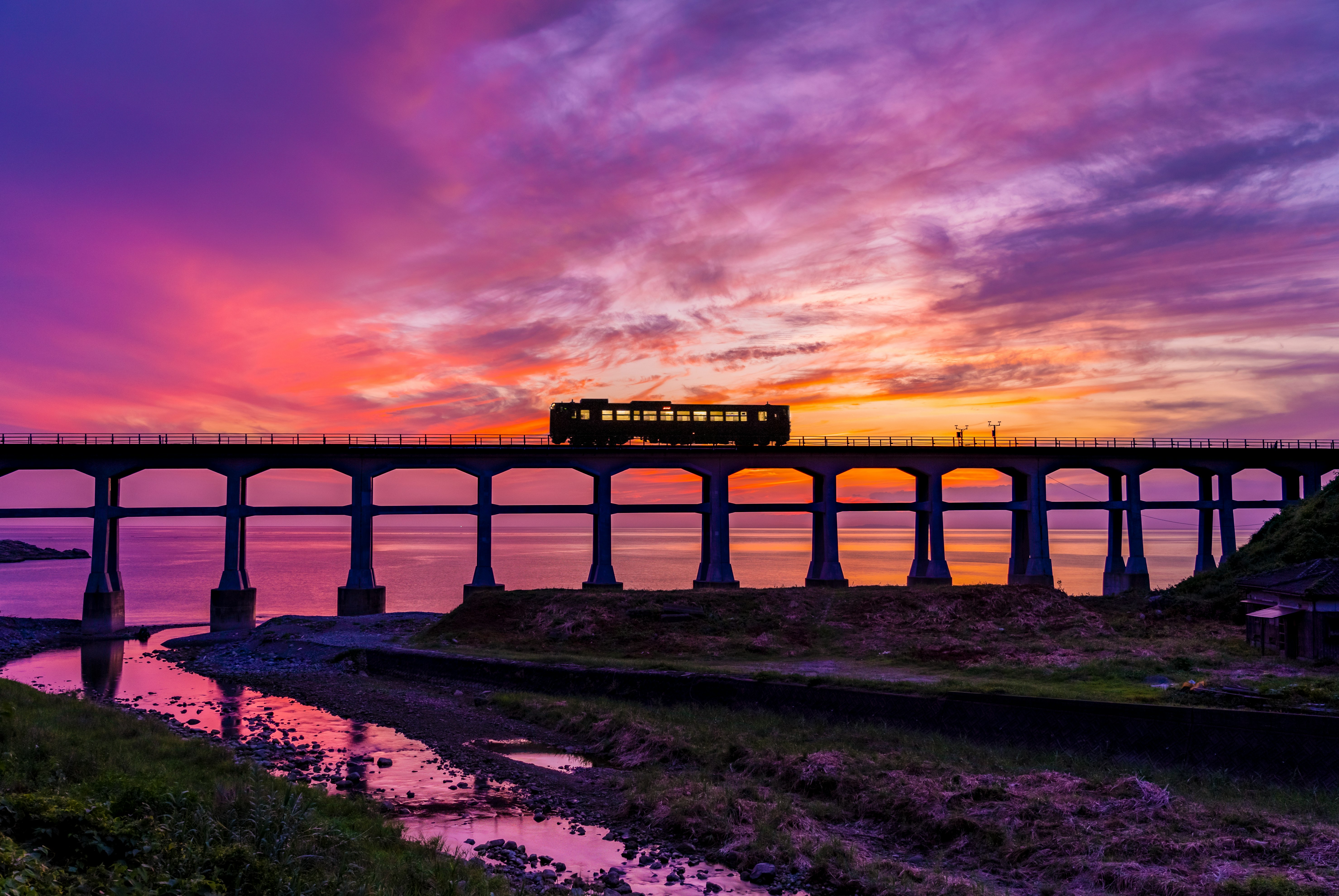 夕焼け空の下を走る列車と海沿いの高架橋