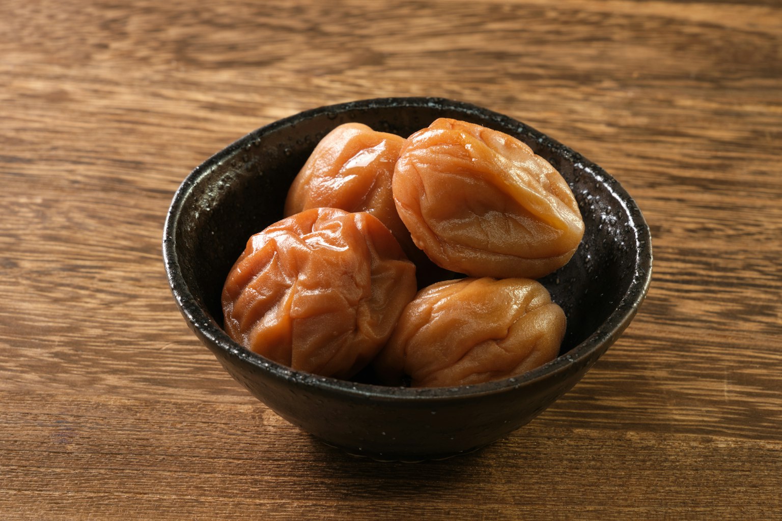 黑色碗中的梅子在木质表面上