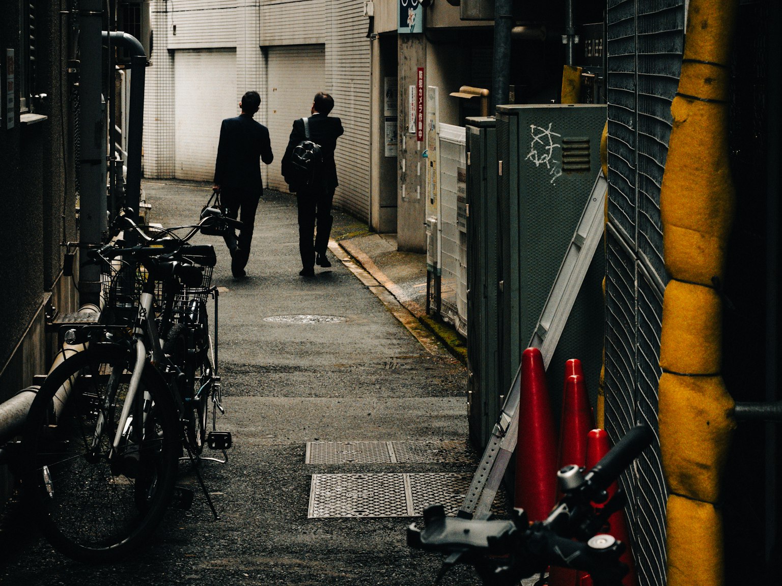 Two businessmen walking in a narrow alley with bicycles