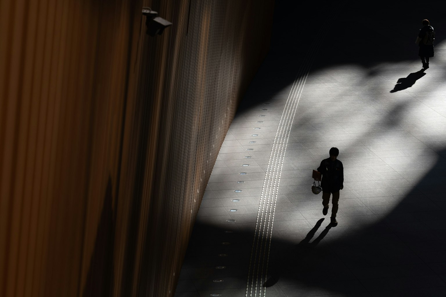 Siluetas de personas caminando en una escena urbana de luz y sombra contrastantes