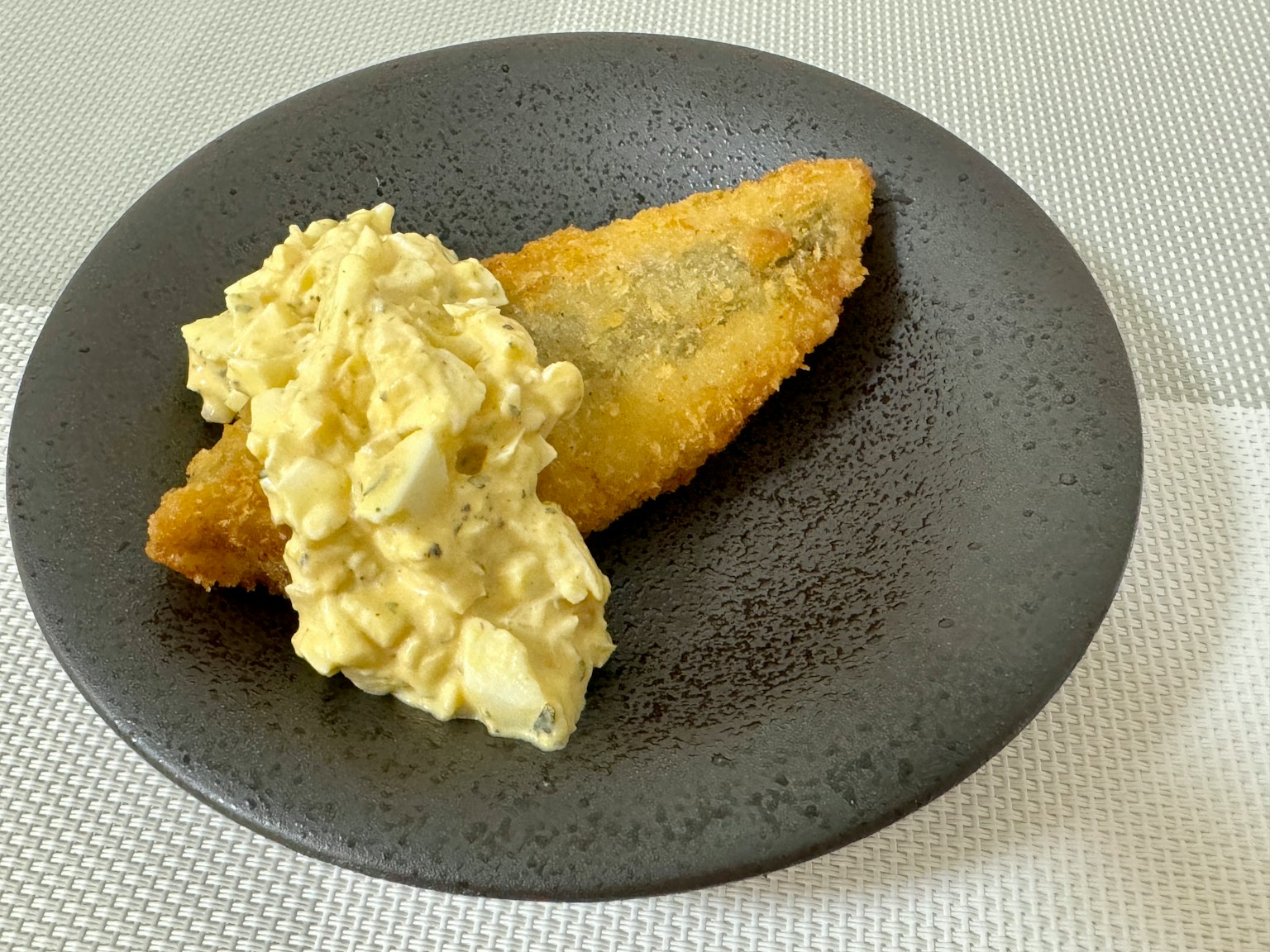 Frittierter Fischfilet mit cremigem Kartoffelsalat auf einem schwarzen Teller