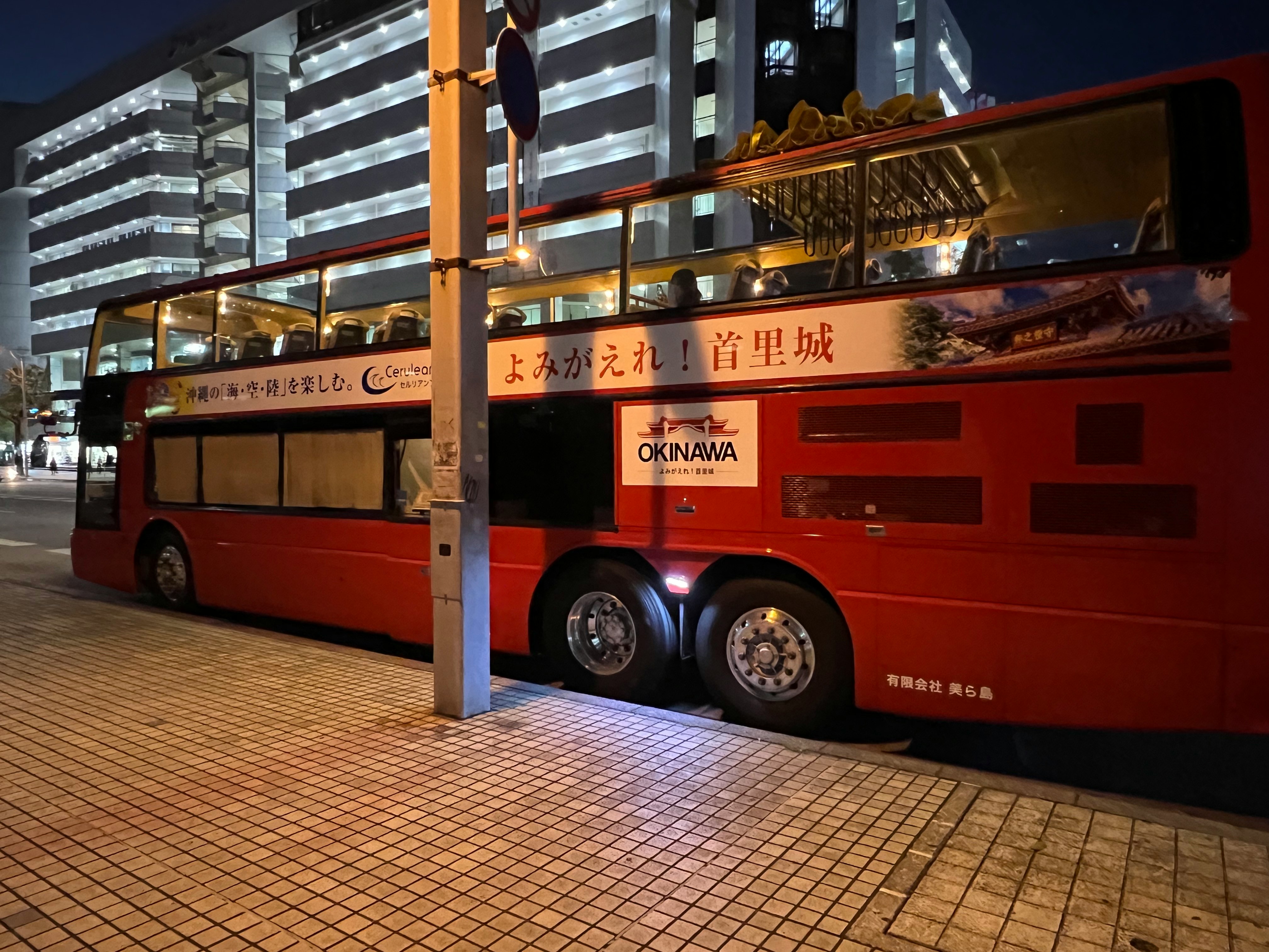 Red sightseeing bus parked at a night bus stop