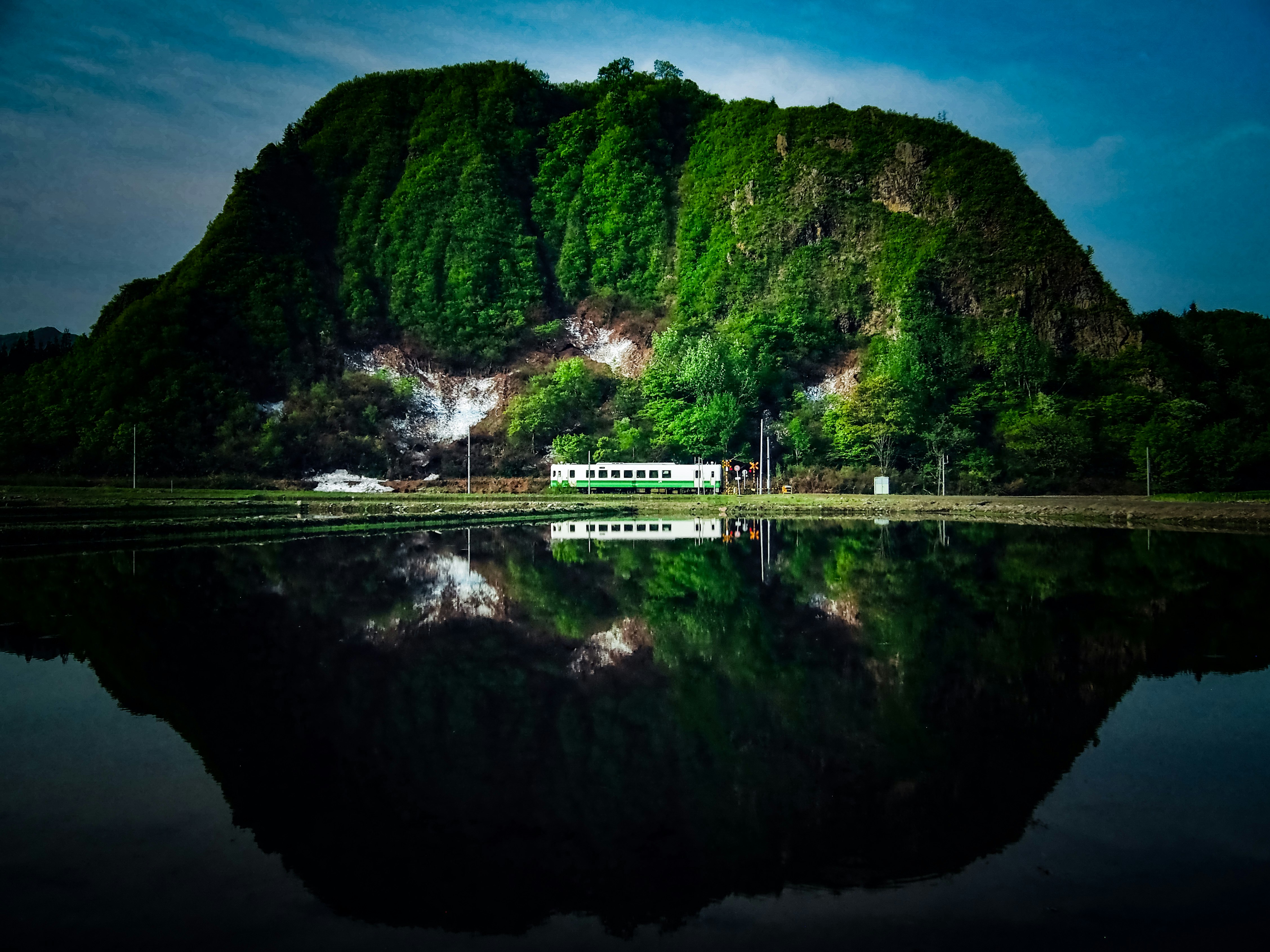 ภาพทิวทัศน์ภูเขาสีเขียวและน้ำตกที่สะท้อนบนผิวน้ำของทะเลสาบ