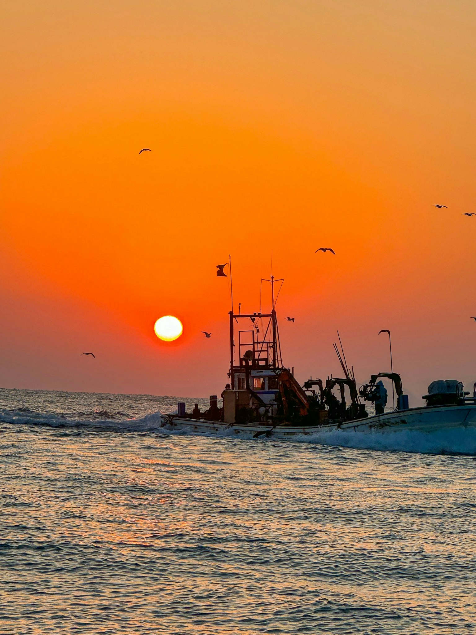 Bateau de pêche silhouetté contre un coucher de soleil vibrant sur l'océan