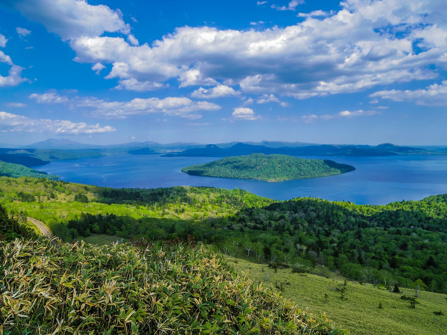 Vue panoramique d'un lac bleu avec des îles vertes sous un ciel clair avec des nuages blancs