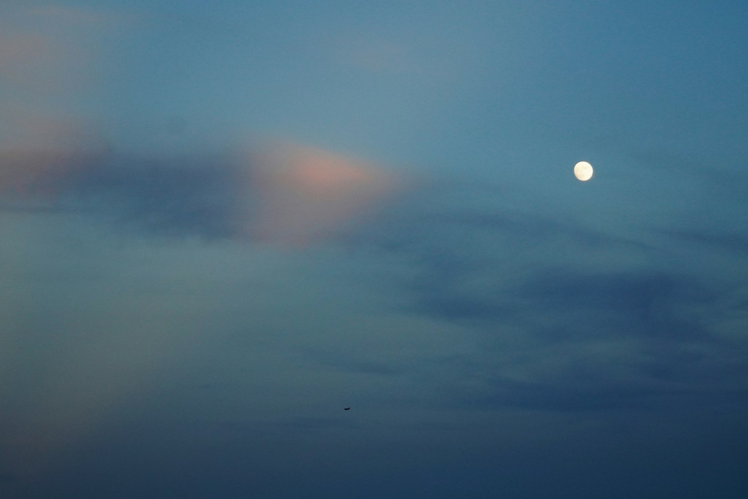 Bright moon in a blue sky with soft clouds