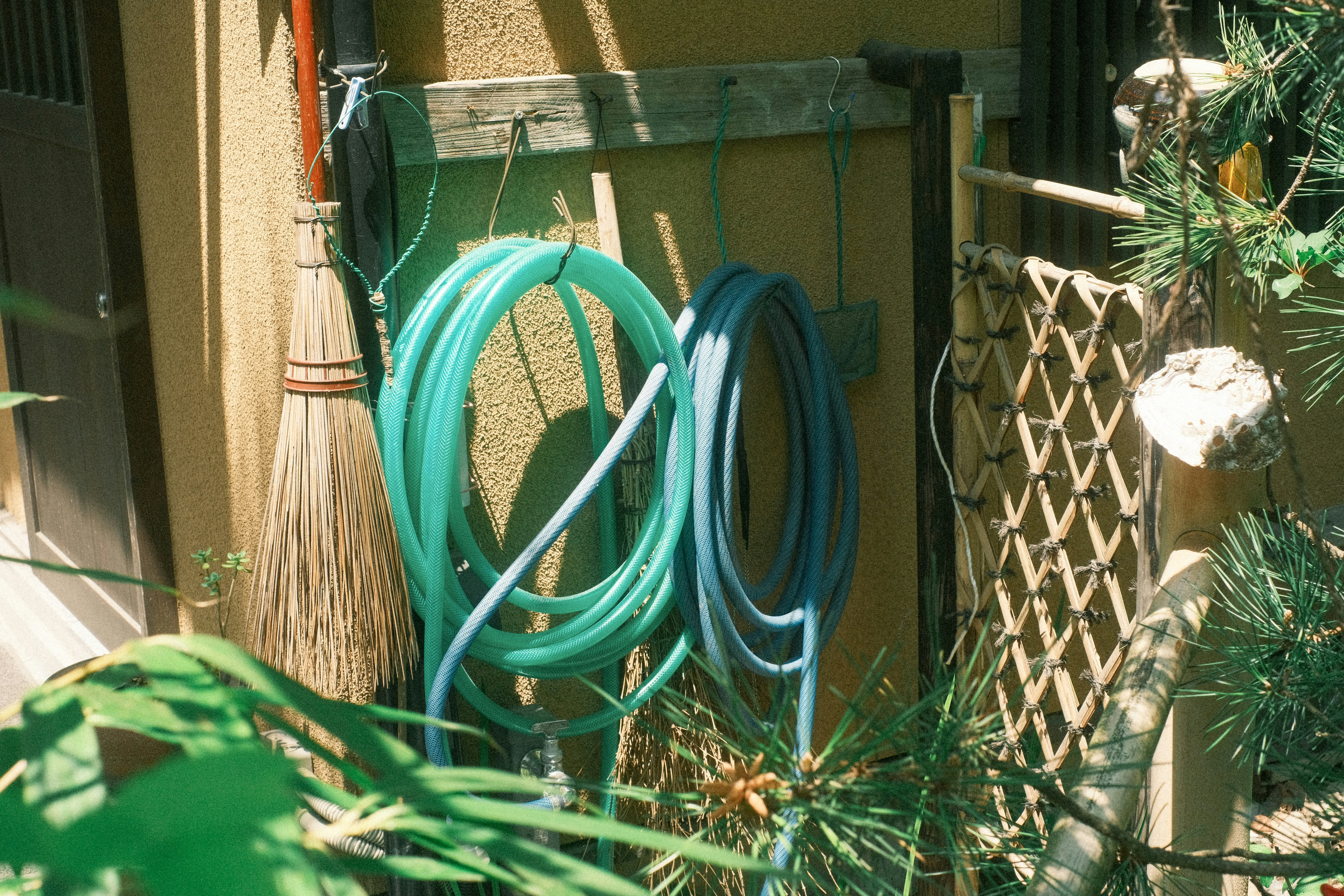green garden hose coiled beside outdoor wall and tools