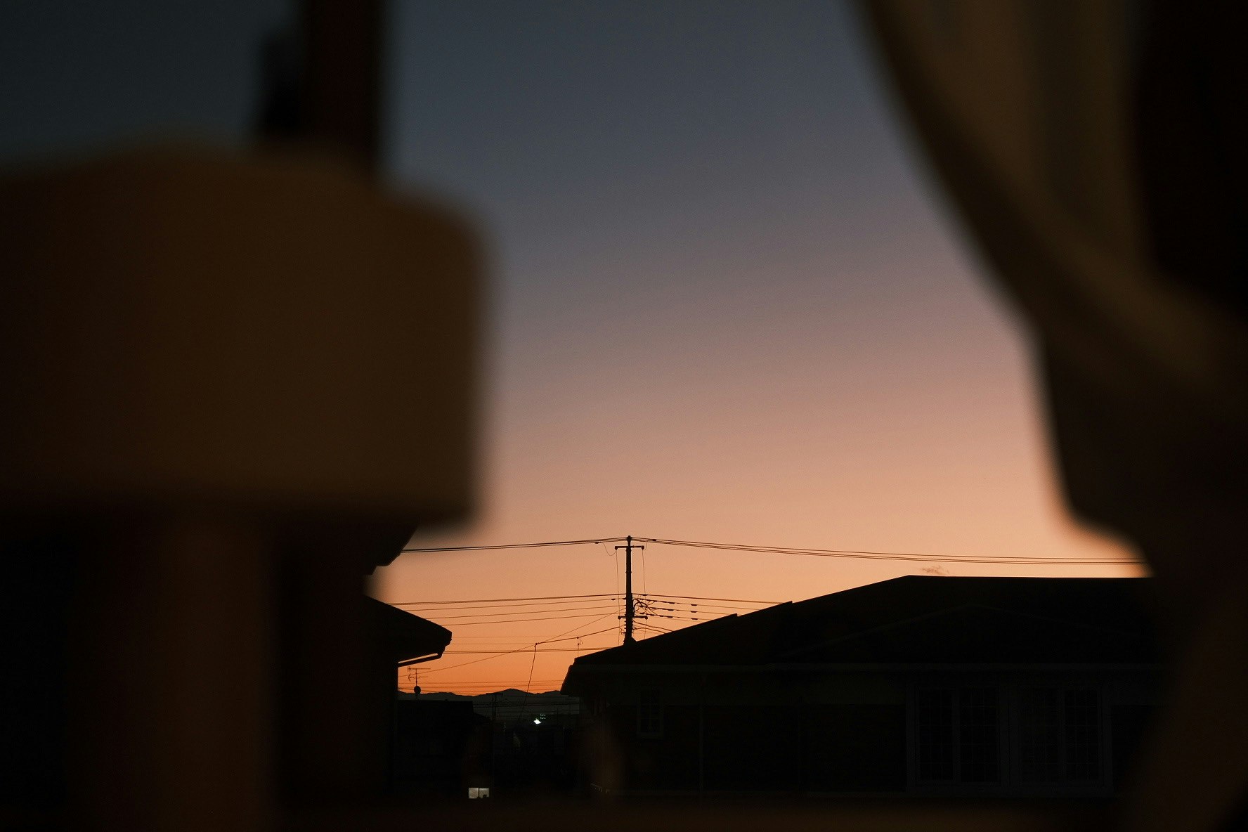 夕暮れの空を窓越しに切り取る路地の景色