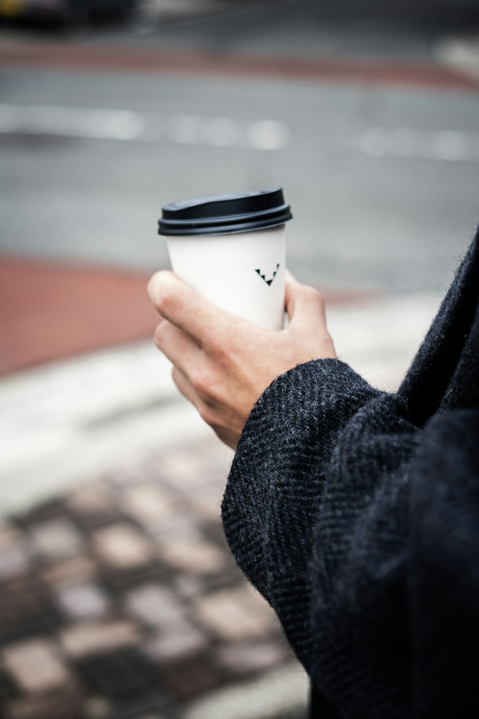 Personne tenant une tasse de café avec un couvercle noir dans un cadre décontracté