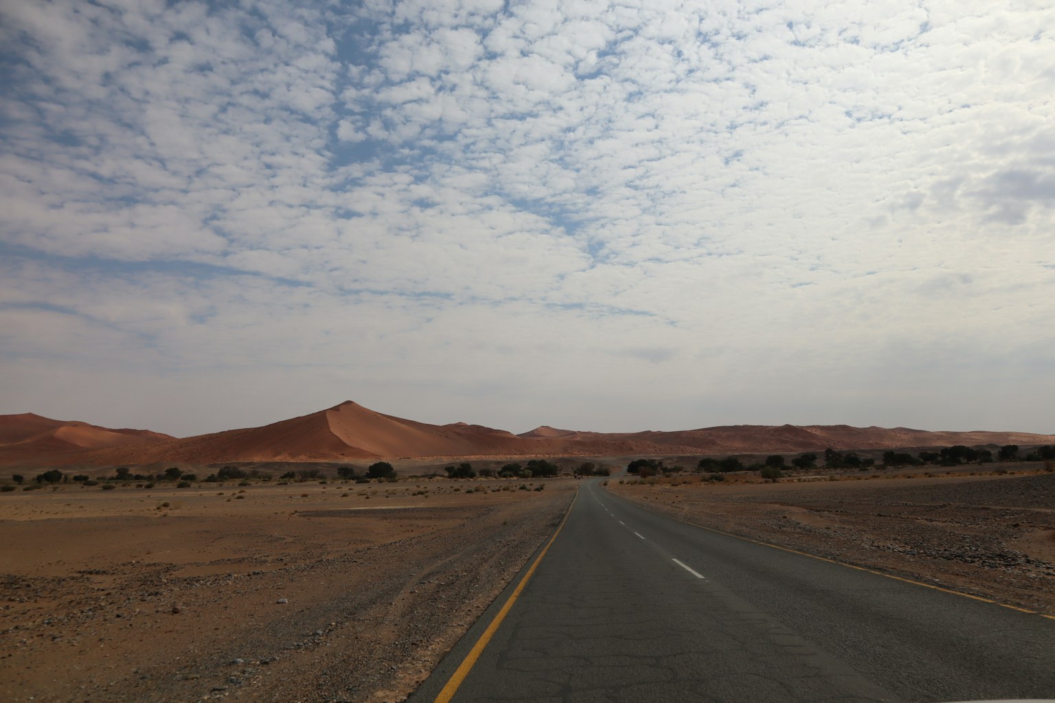 Strada nel deserto con colline rosse in lontananza sotto un cielo nuvoloso