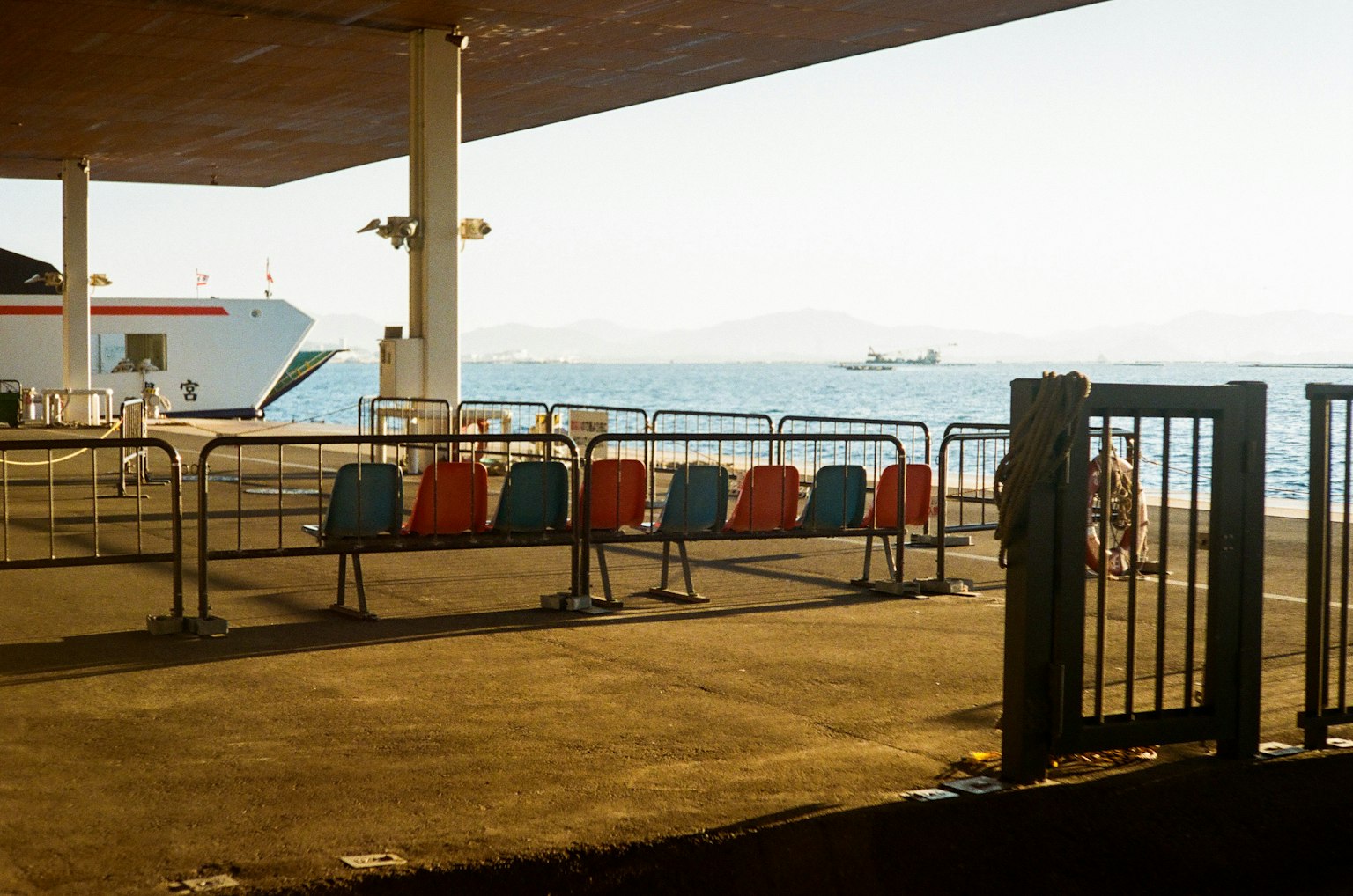 Chaises rouges et bleues alignées dans une zone d'attente au bord de la mer dans un port