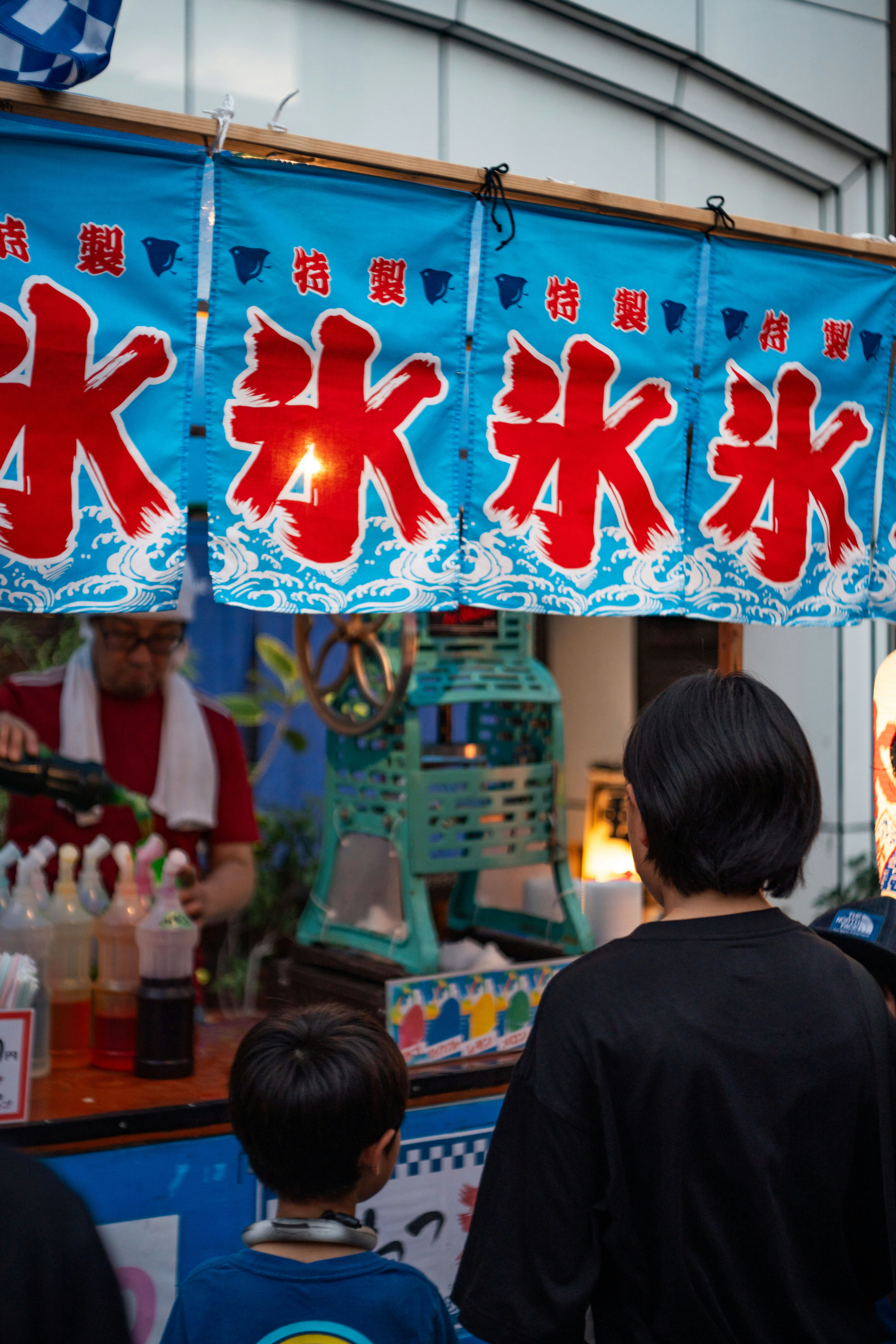 青い屋台の暖簾と「特製」看板のある祭りの屋台前