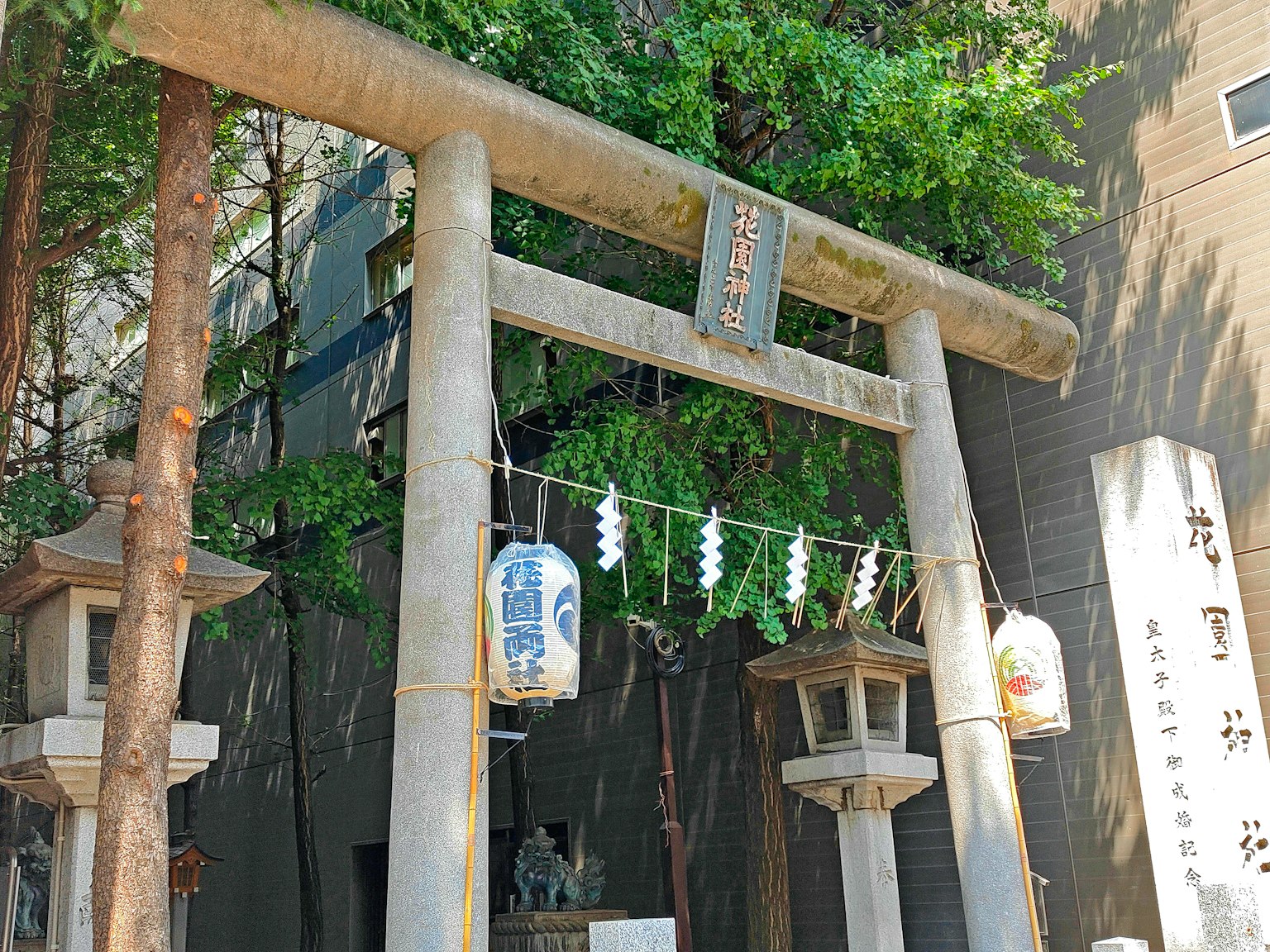 Entrata di un santuario con un torii e lanterne circondate da vegetazione