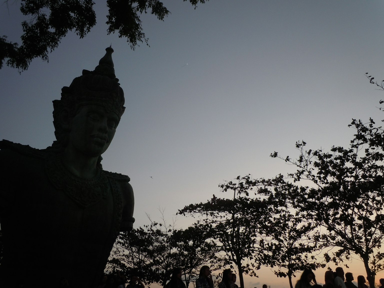 Silhouette d'une statue de Bouddha contre un ciel crépusculaire avec des arbres environnants
