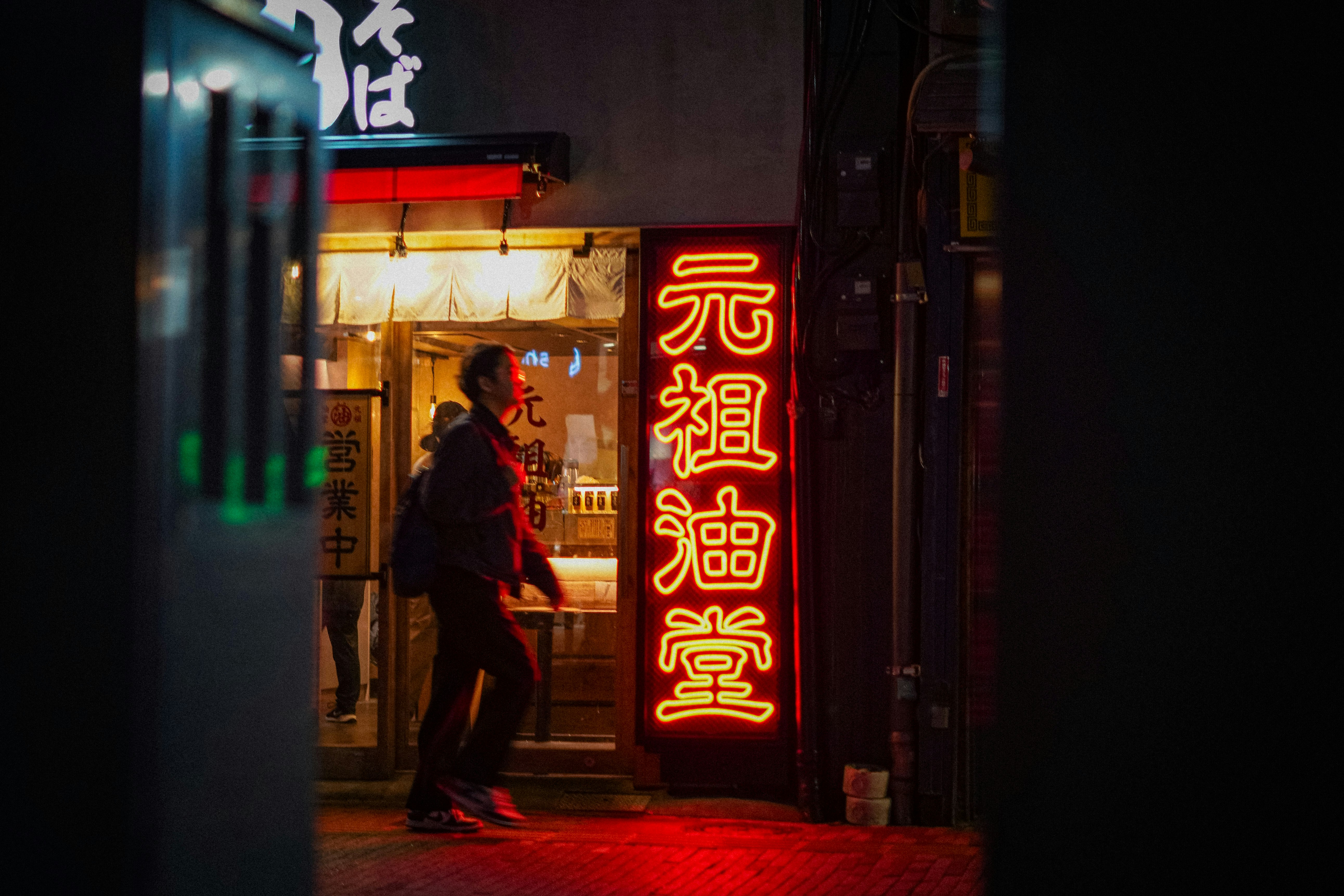 ネオンが灯る路地の飲食店前で立つ人物