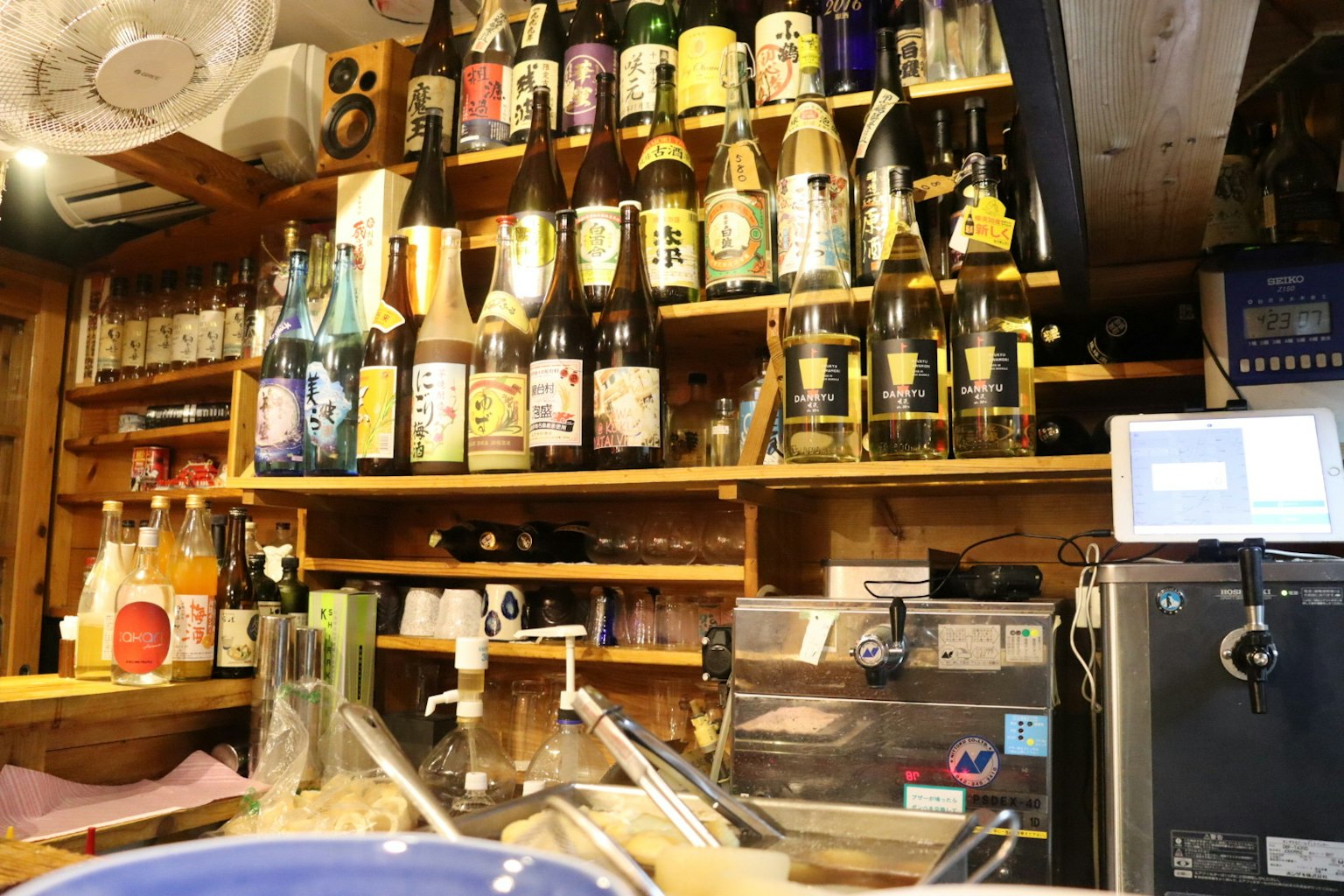 Interior de un izakaya con estantes de botellas de sake y un mostrador