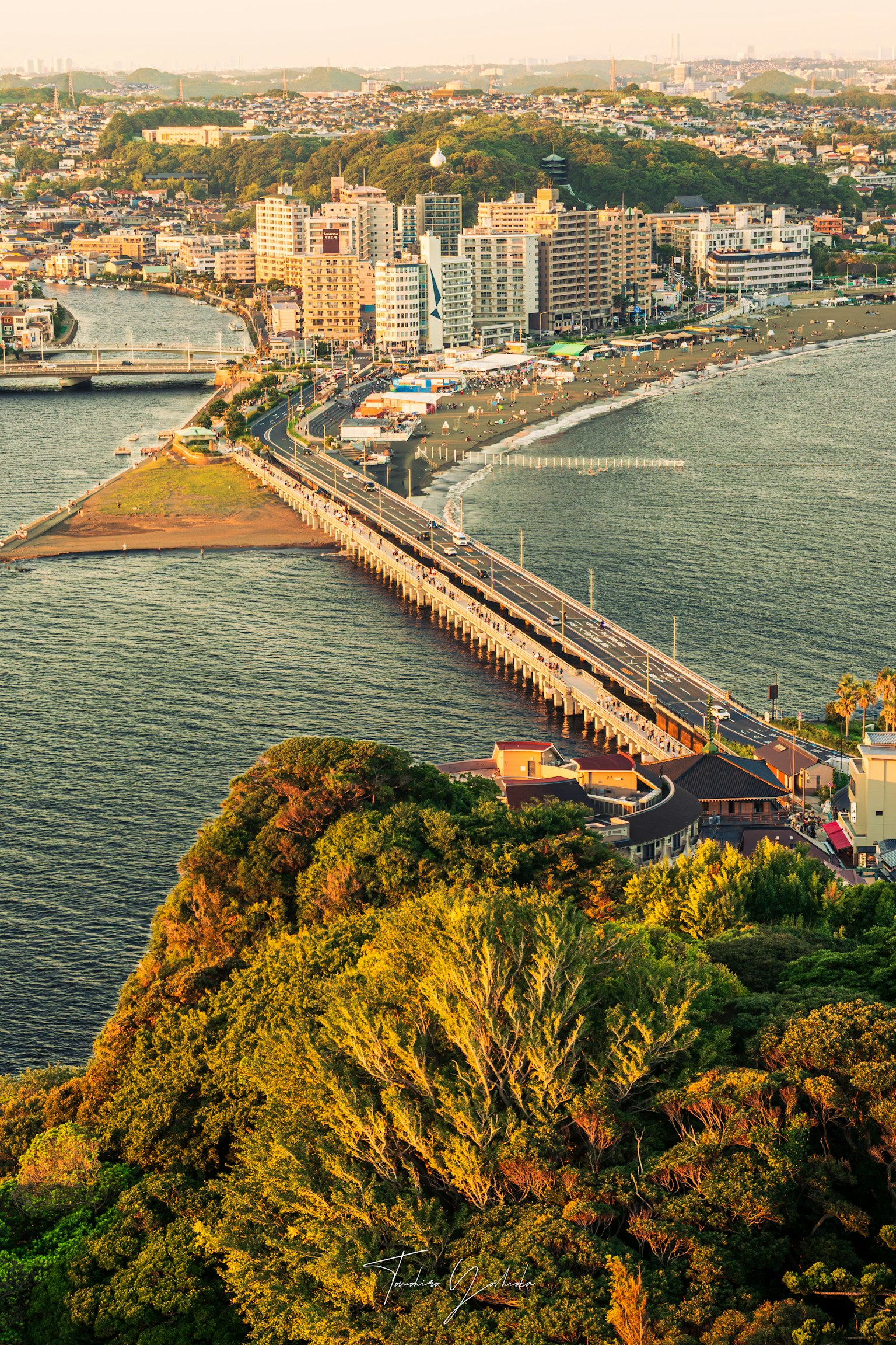 海岸城市與橋樑連接的鳥瞰圖 周圍環繞著水和綠樹的日落