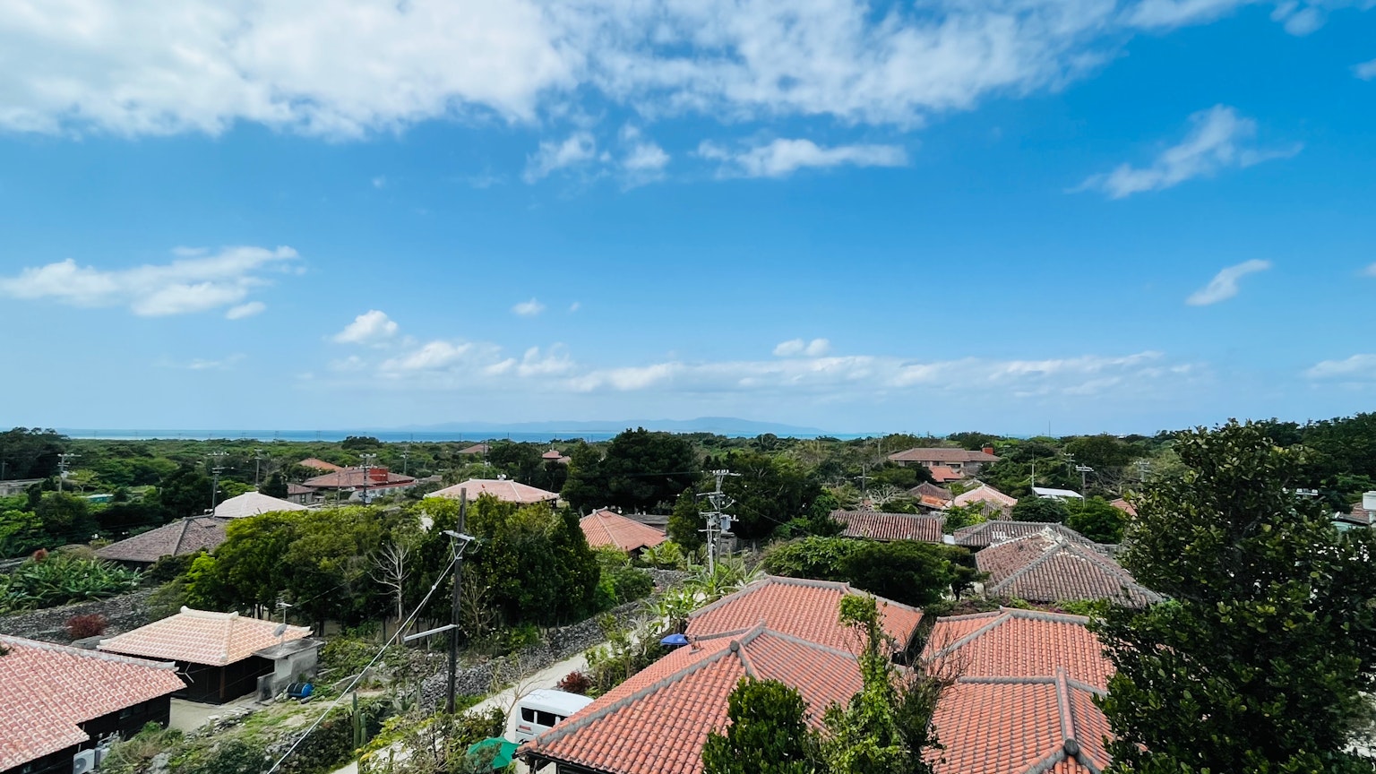 Vista panoramica di un'area residenziale sotto un cielo blu con nuvole bianche caratterizzata da tetti in tegole rosse e alberi verdi
