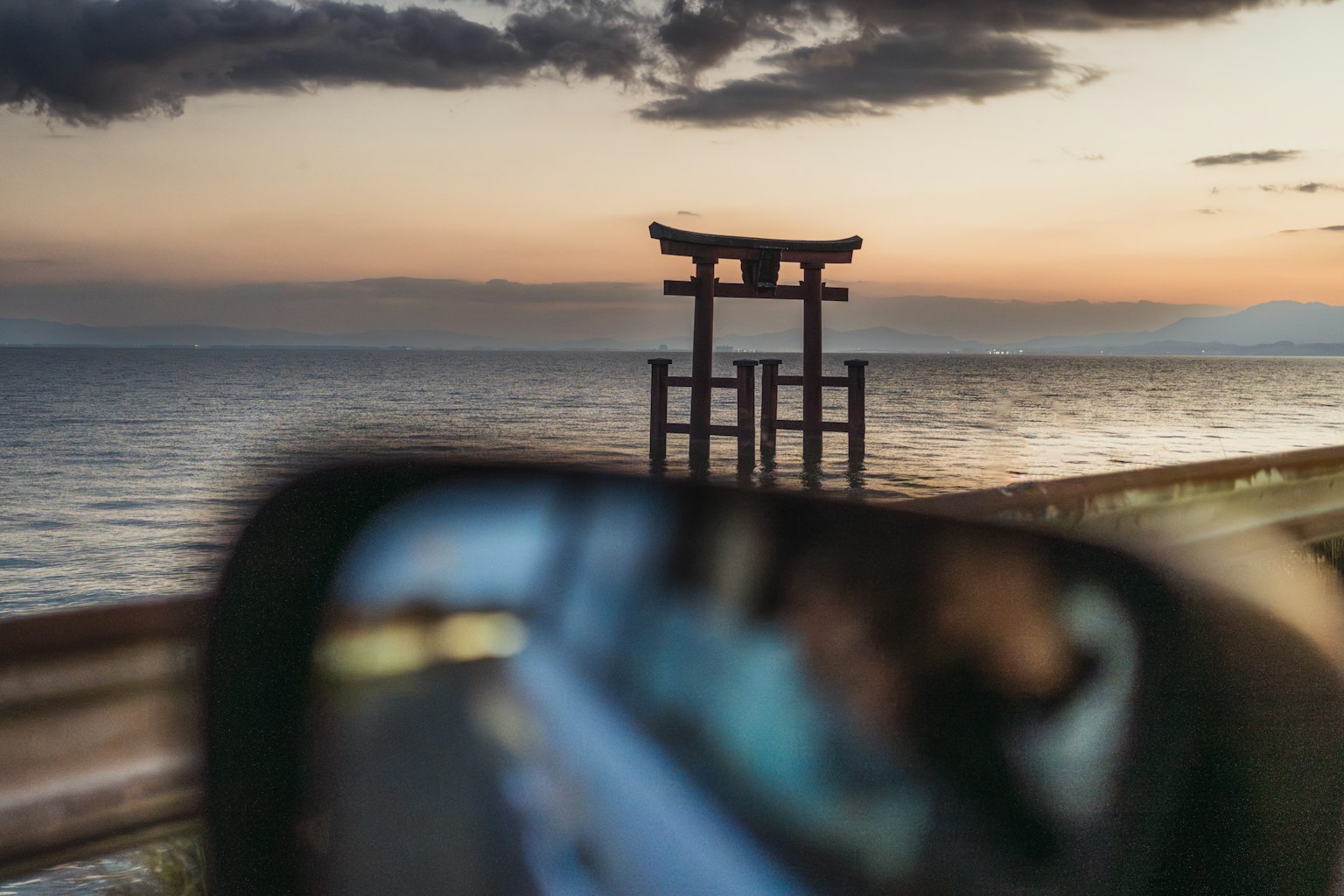 Torii dekat laut saat matahari terbenam tercermin di kaca spion mobil