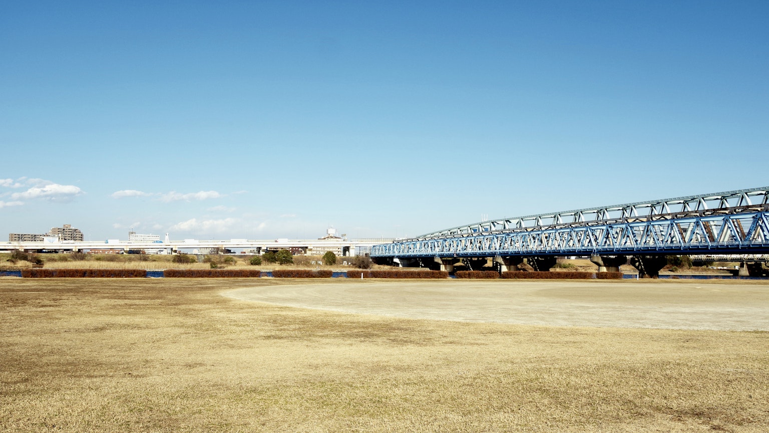 Jembatan baja biru di bawah langit cerah dengan padang rumput kering