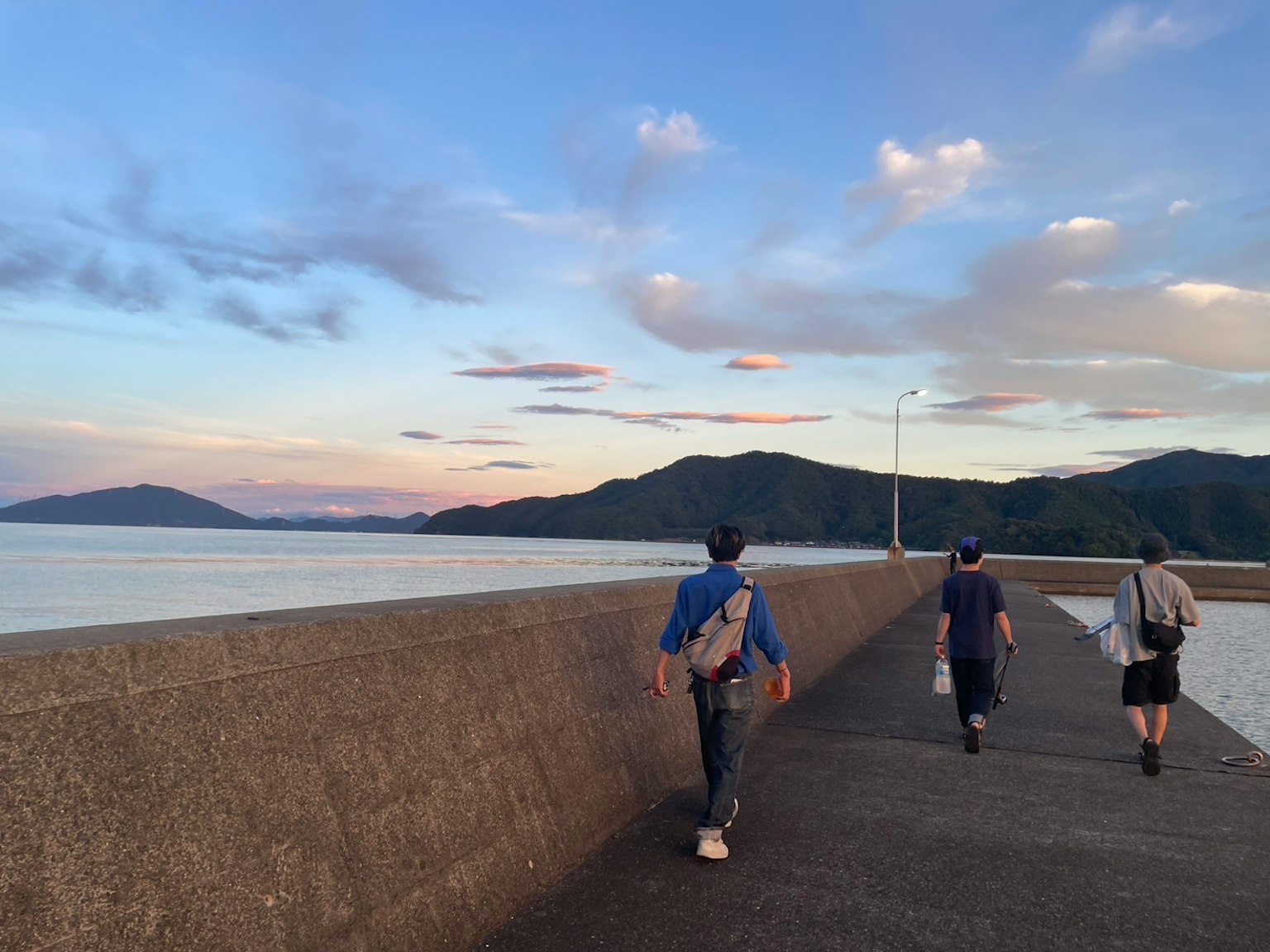三个人在海边的堤坝上散步，背景是美丽的日落天空