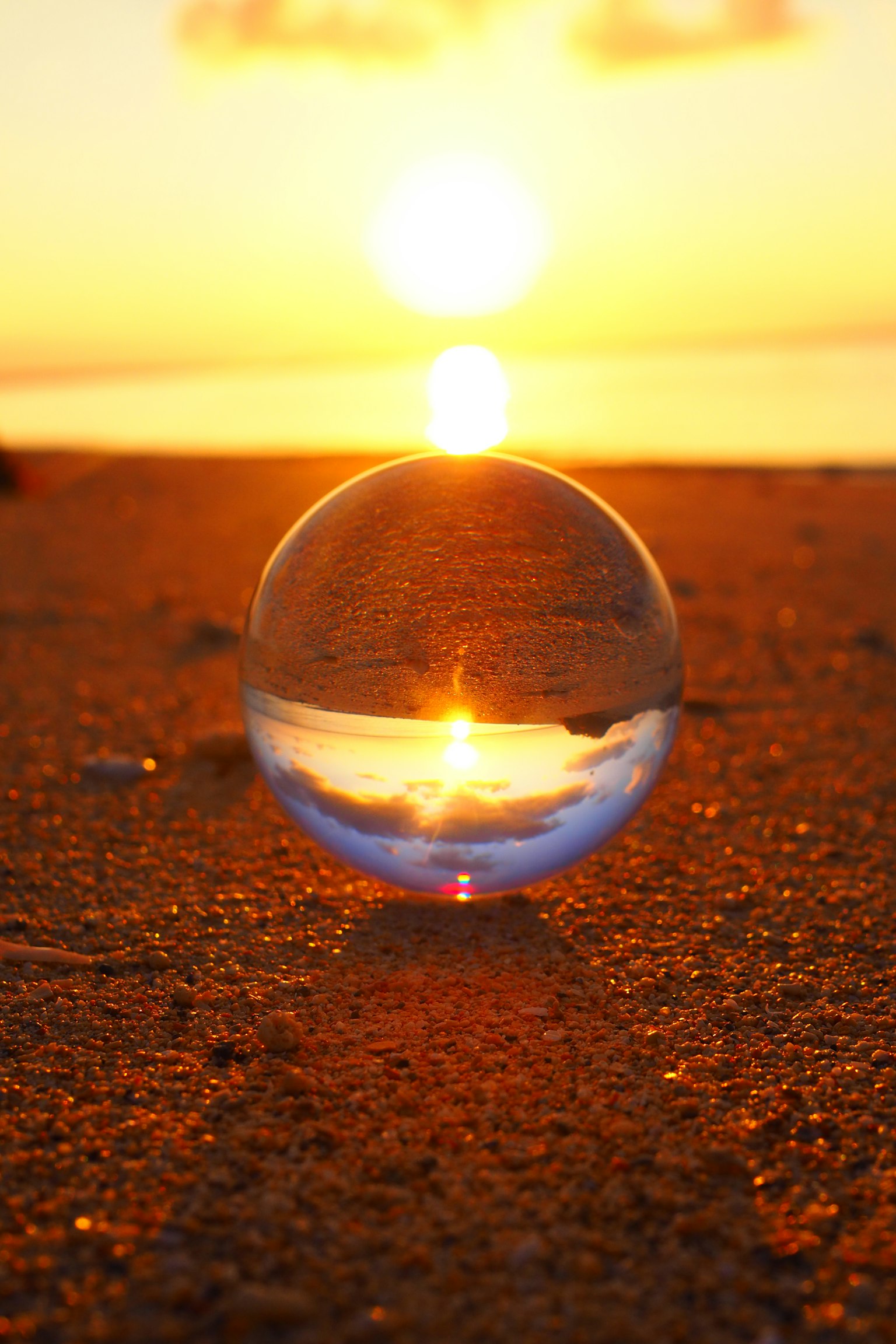 Transparente Glaskugel, die den Sonnenuntergang an einem Sandstrand reflektiert
