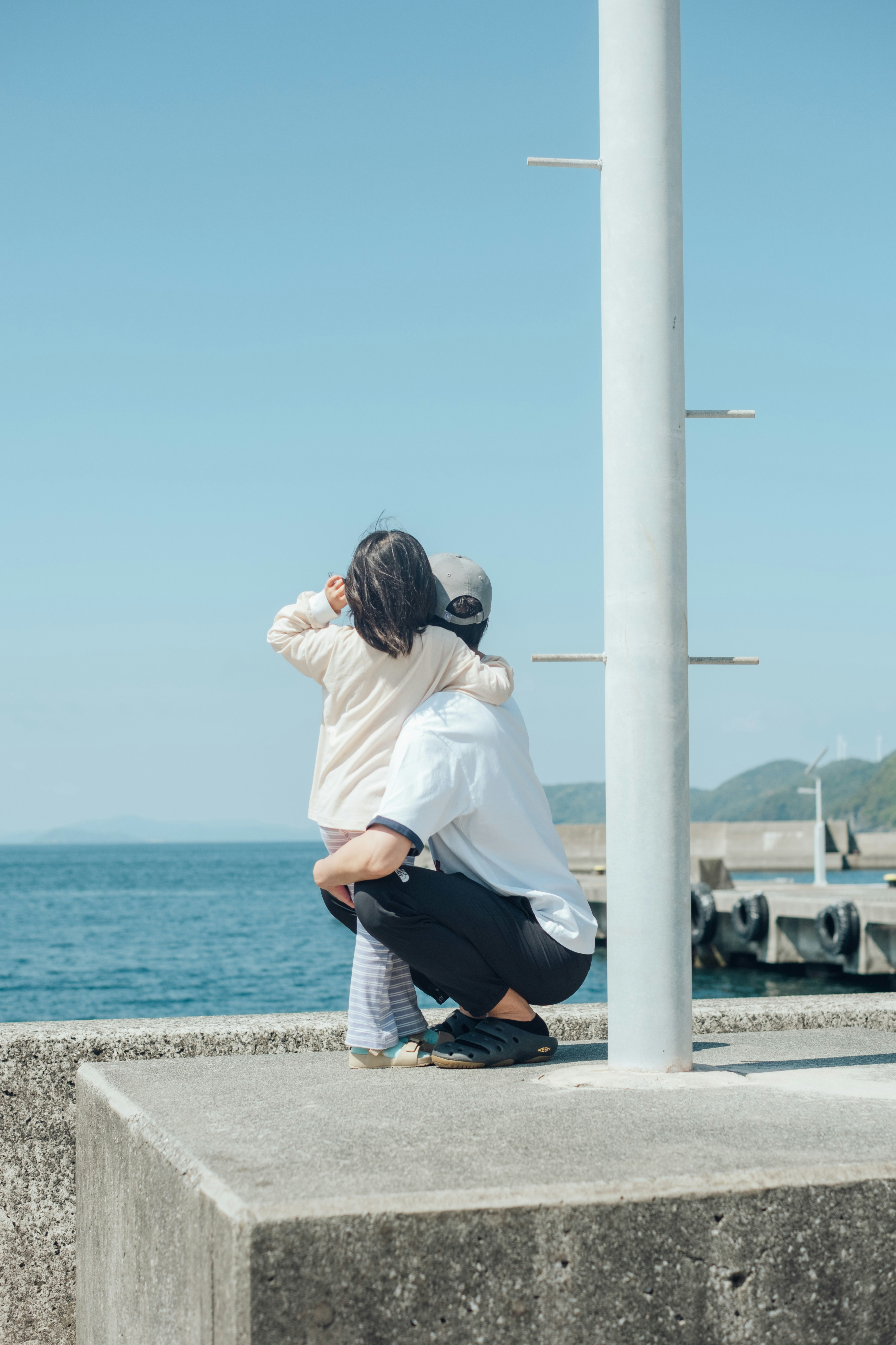 青い空の下で海辺の防波堤に寄り添う親子