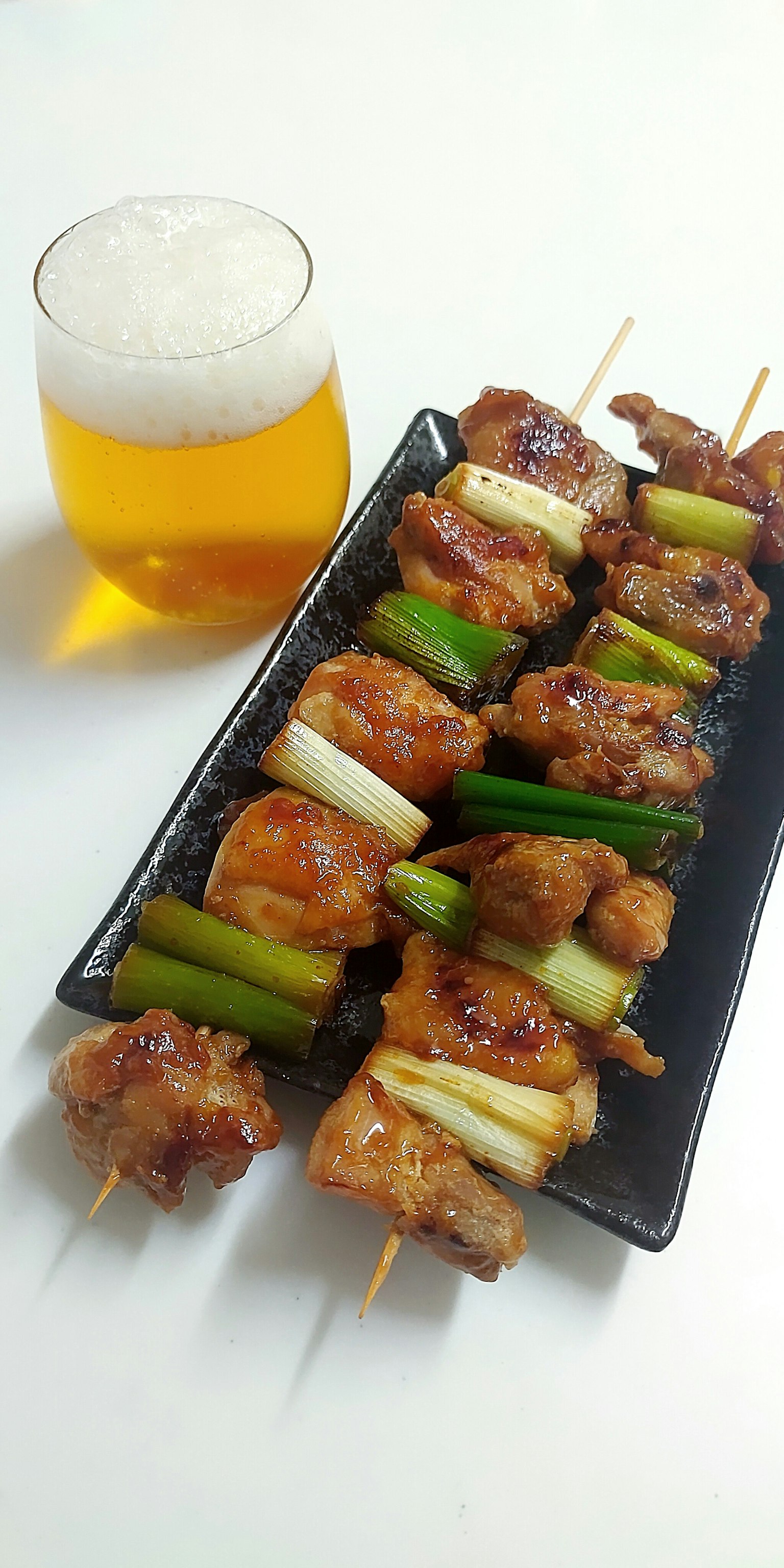烤雞肉和青蔥串放在盤子上，旁邊是一杯啤酒