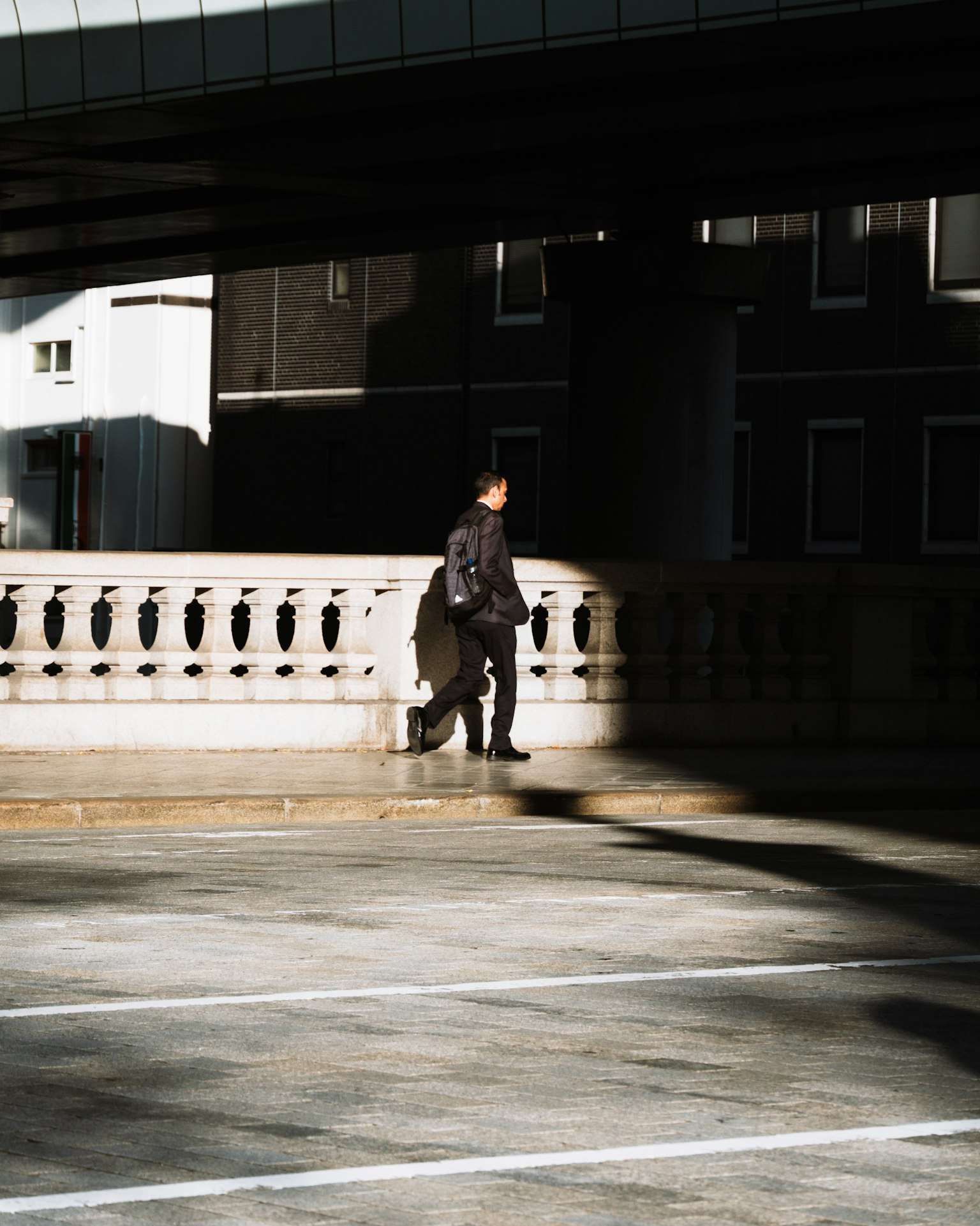 Una silueta de una persona vestida de negro caminando sobre un puente con sombras contrastantes